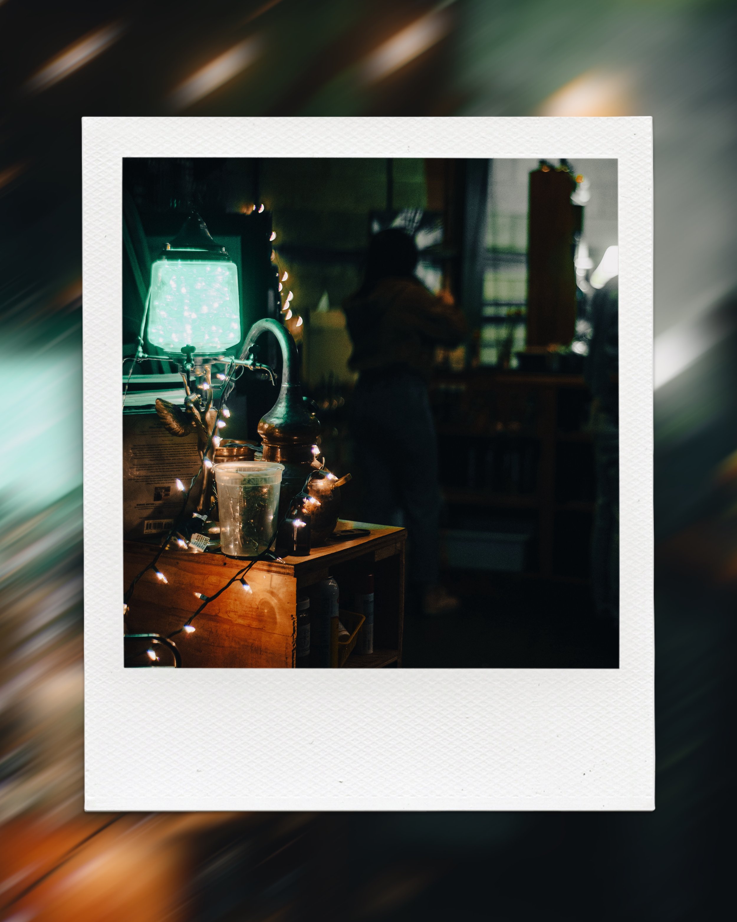 Vintage room interior with dim lighting, featuring a green lampshade, copper kettle, string lights, and blurred background including a person standing by a window.
