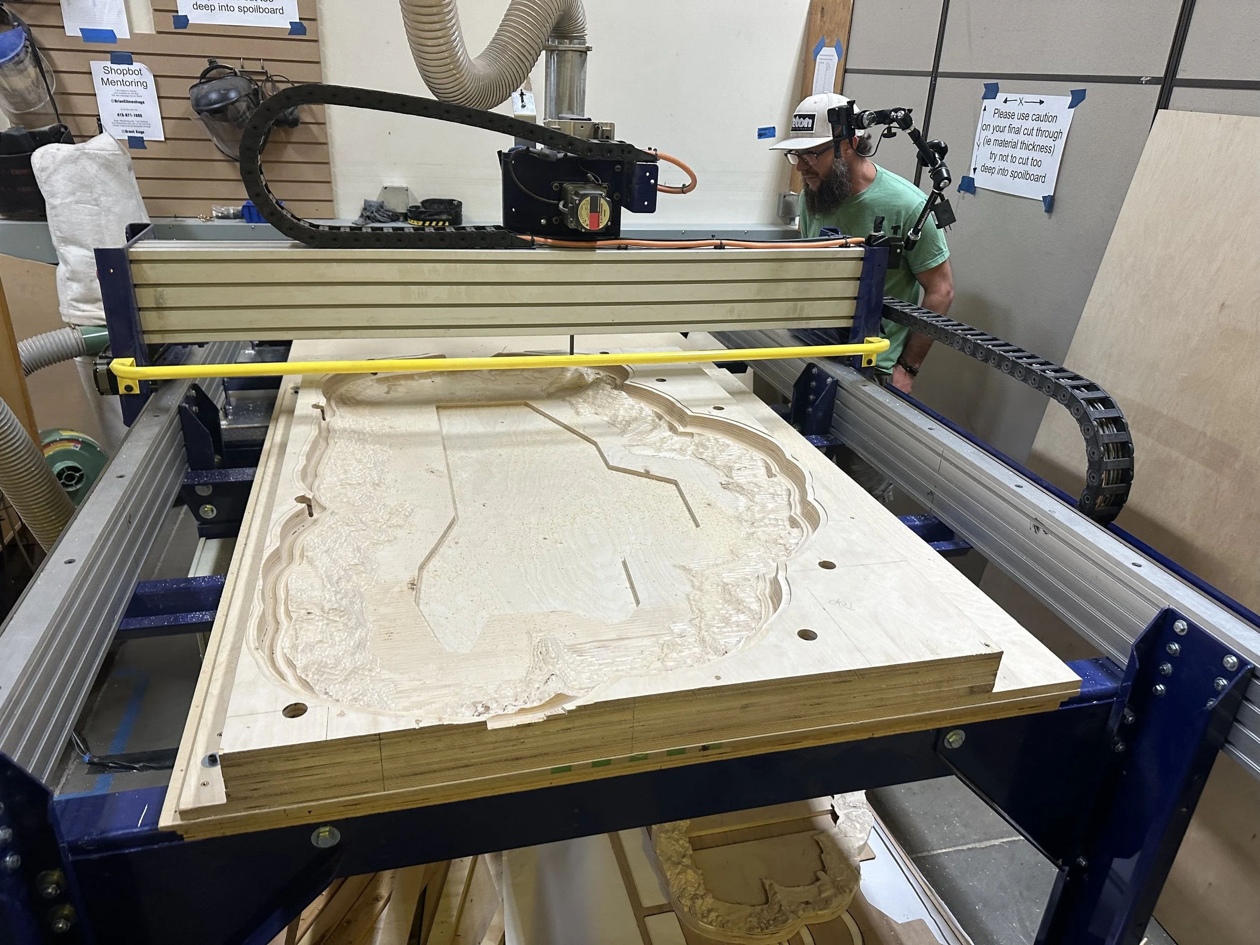 Person operating a CNC machine carving a detailed design into a large wooden panel in a woodworking workshop.