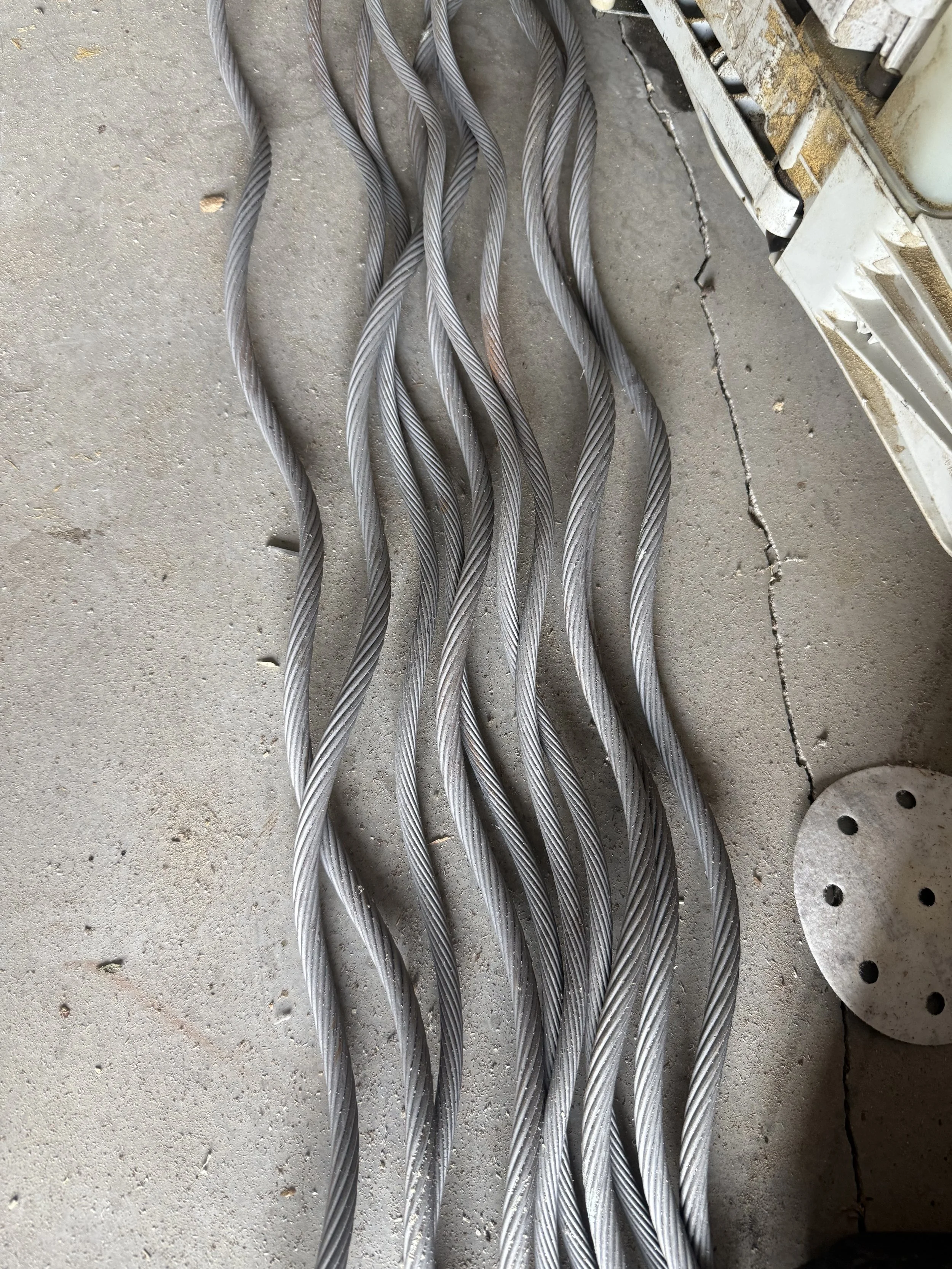Multiple twisted steel cables laid out on a concrete floor.