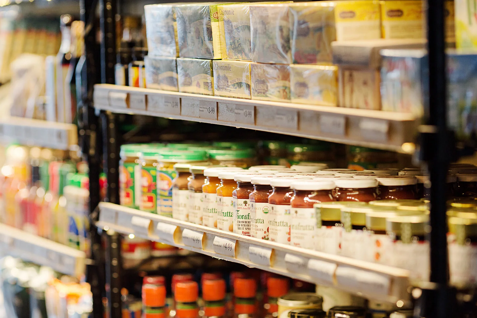 Shelves stocked with jars of fruit spread and boxes of herbal tea in a grocery store.