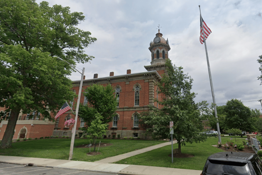 Historic Geauga County Courthouse in Chardon, Ohio, featuring a red-brick exterior, clock tower, landscaped grounds, and American flags surrounding the courthouse.