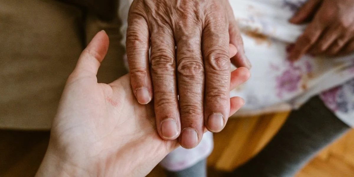 Close-up of an older adult's hand resting on a younger person's hand, symbolizing caregiving, support, and long-term planning.