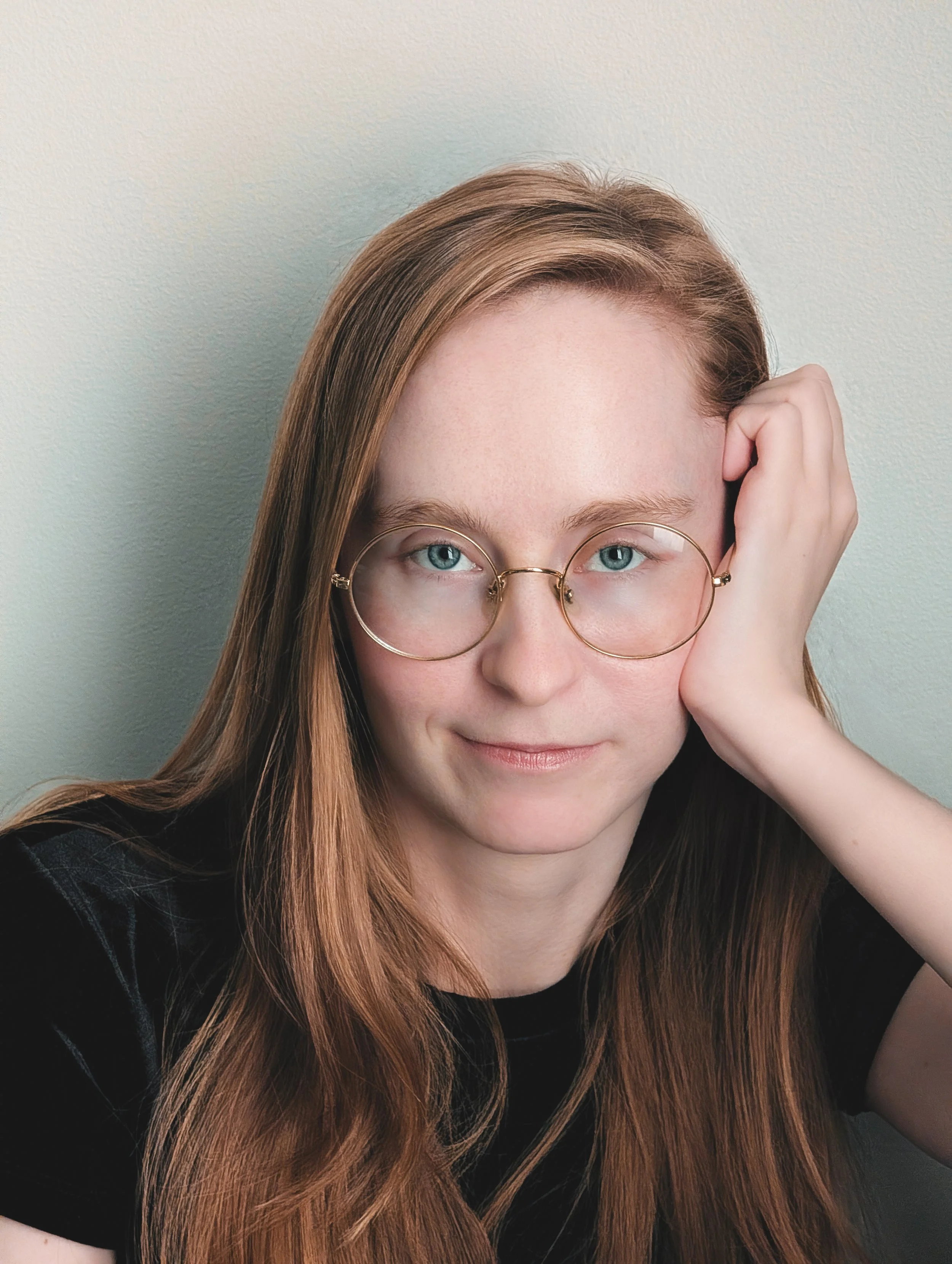Blonde woman with blue eyes and round gold glasses making eye contact with the camera