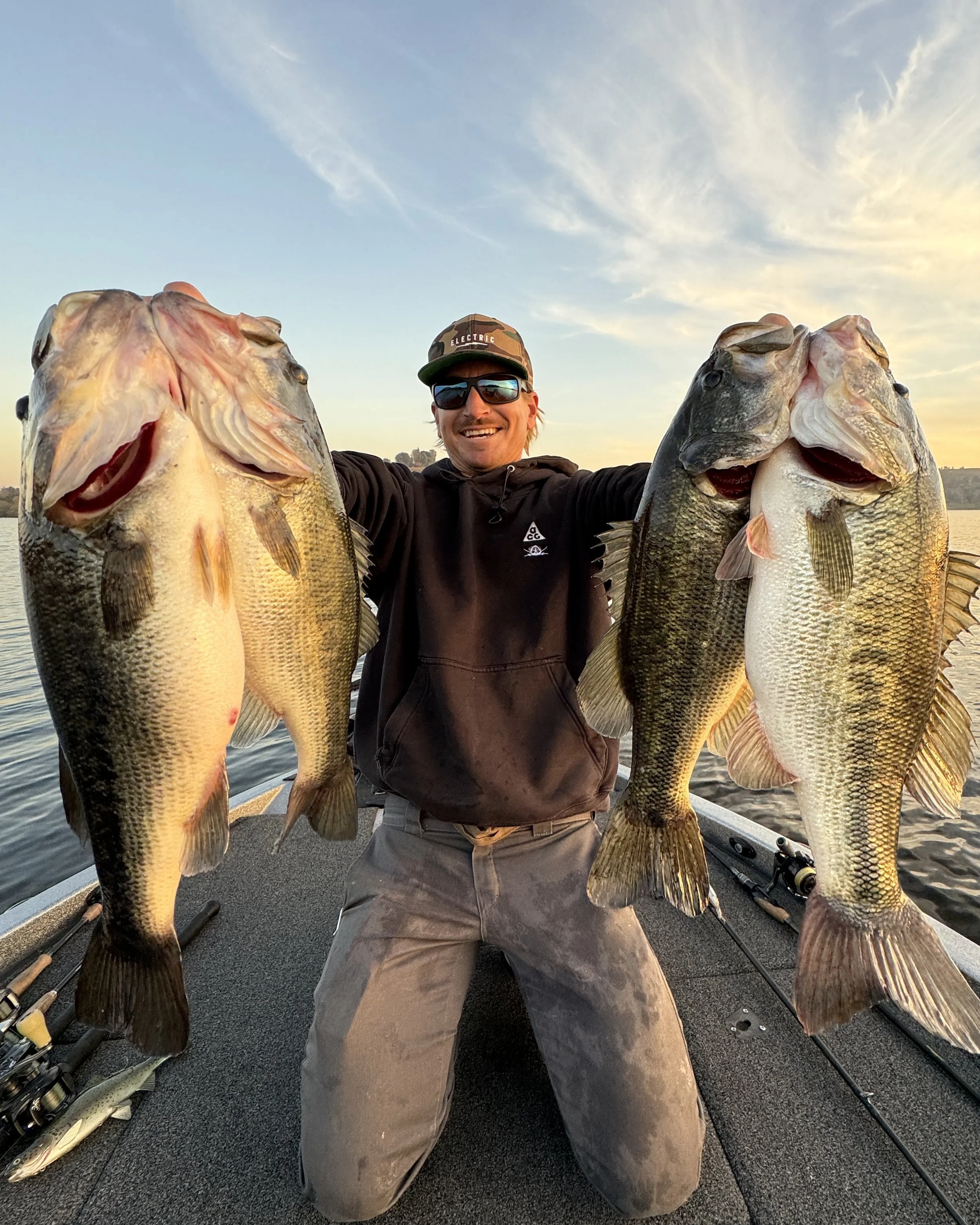Man holding two large bass fish on a boat at sunset.  Puddingstone reservoir bass fishing guide in souther California running trips and charters for fishing.