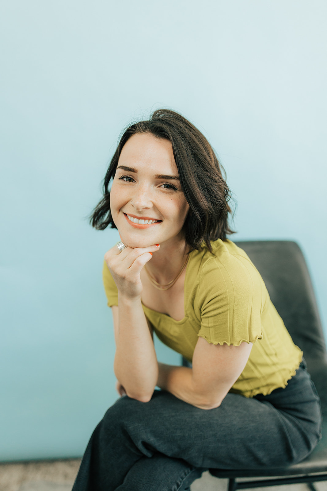 Smiling woman with short dark hair in a yellow top, posing in front of a light blue background.