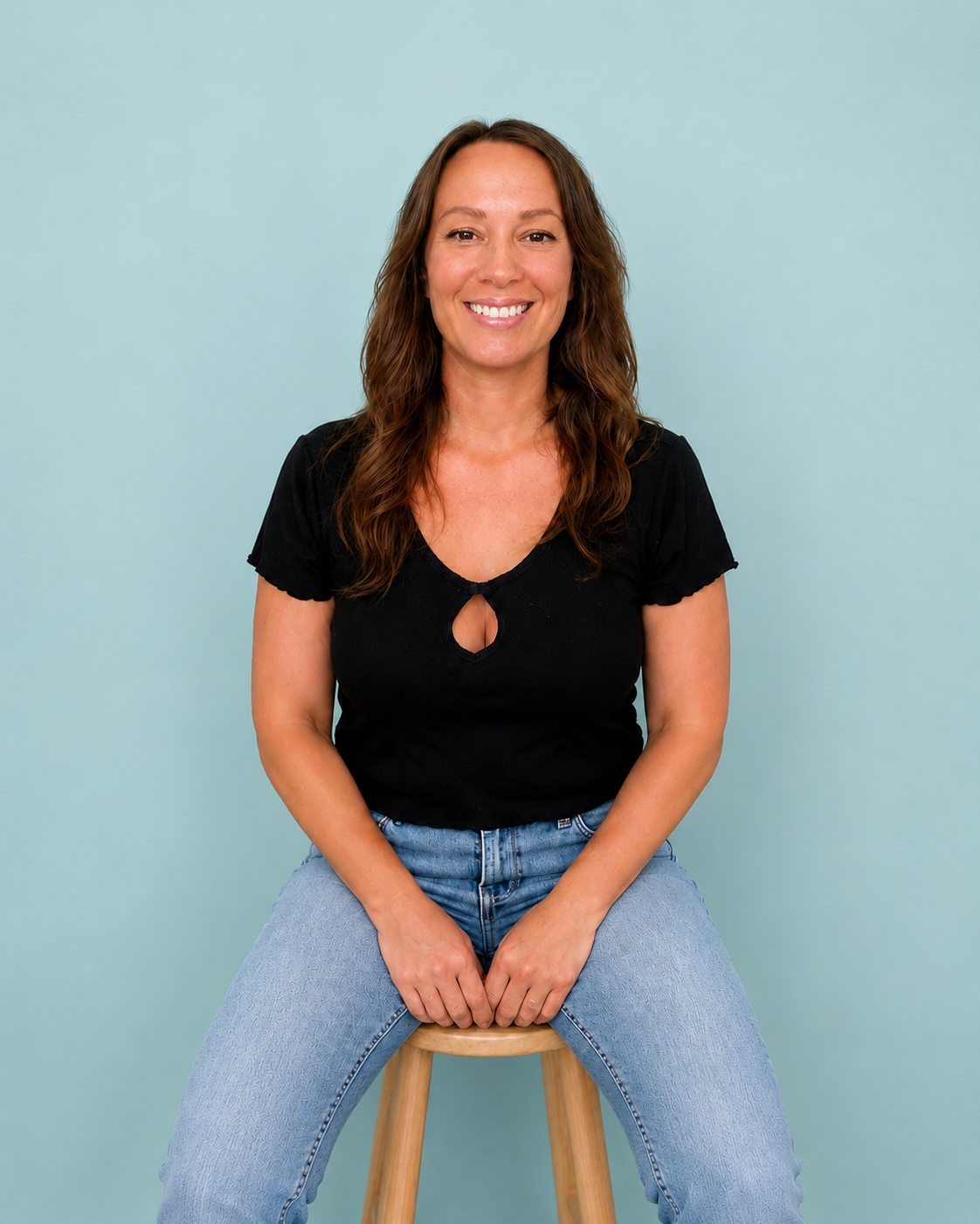 Ginning woman with long dark hair in a black long sleeve top, posing in front of a light green background.
