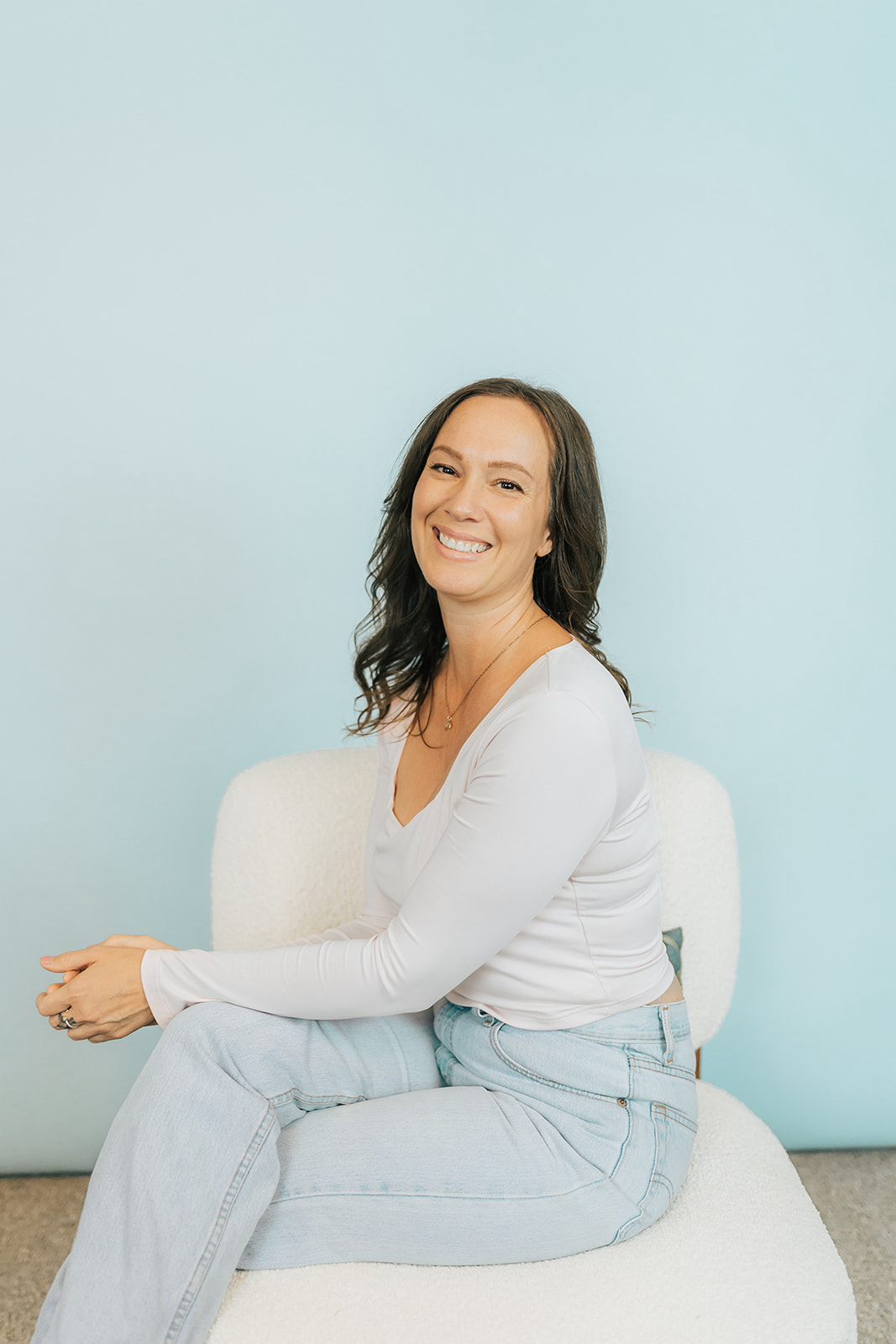 Ginning woman with long dark hair in a black long sleeve top, posing in front of a light green background.