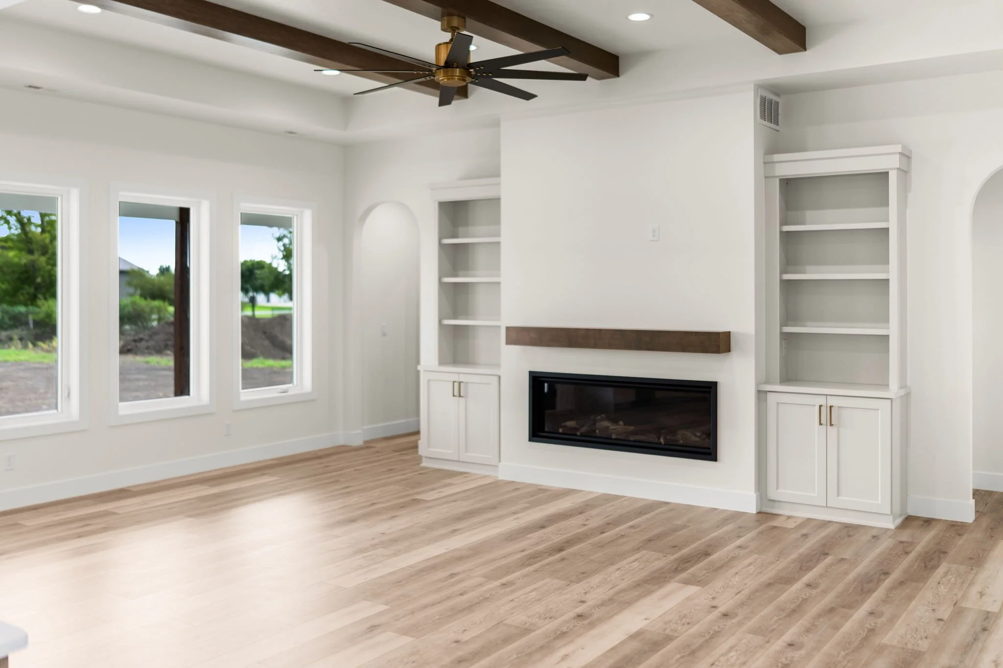 Living room with white walls, large windows, a ceiling fan with black blades, and a modern fireplace surrounded by white cabinetry and open shelves. Hardwood floors.