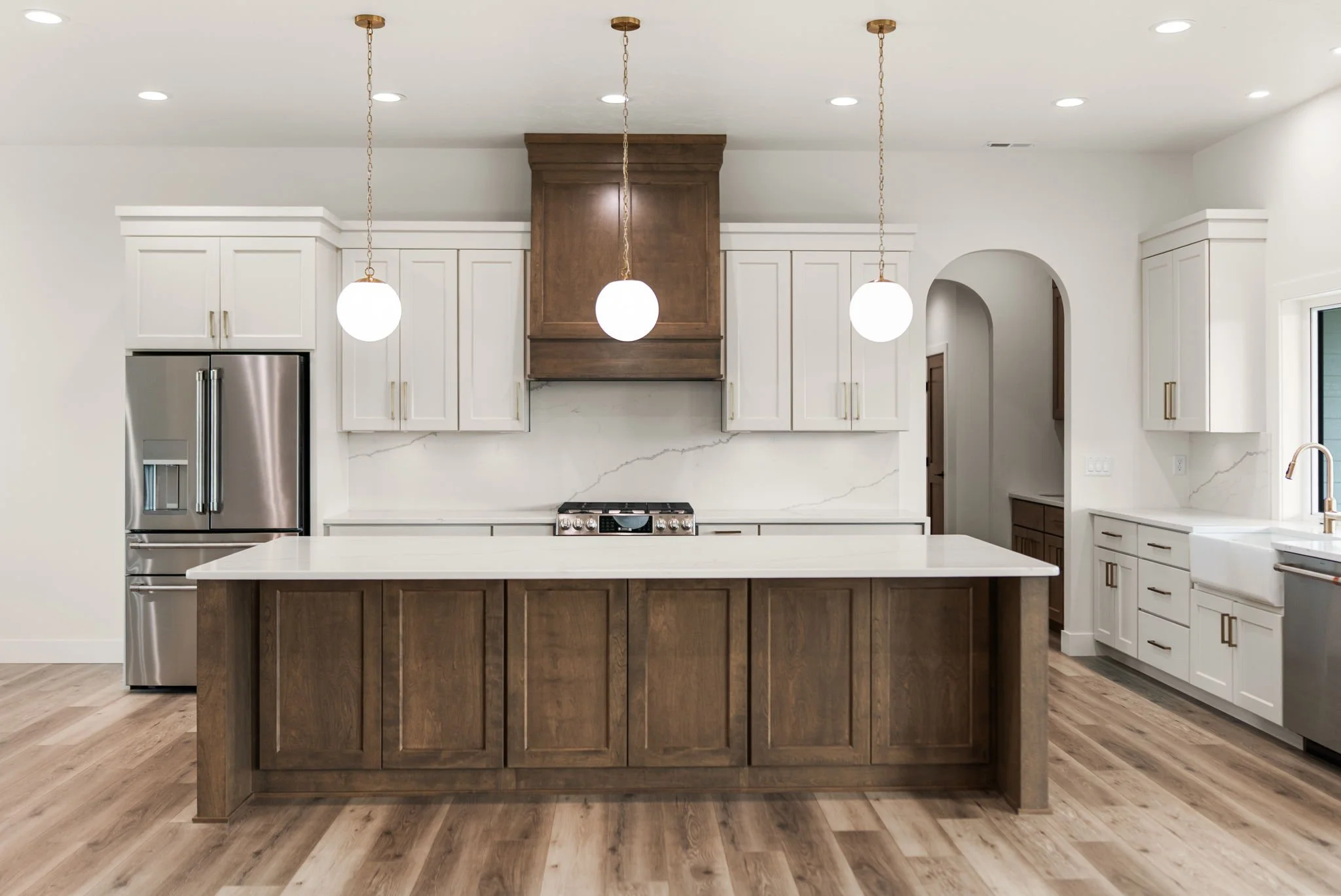 Modern kitchen with white cabinets, a central island with wood finish, stainless steel refrigerator, and pendant lights hanging from the ceiling. There is also a stove and a window nearby.