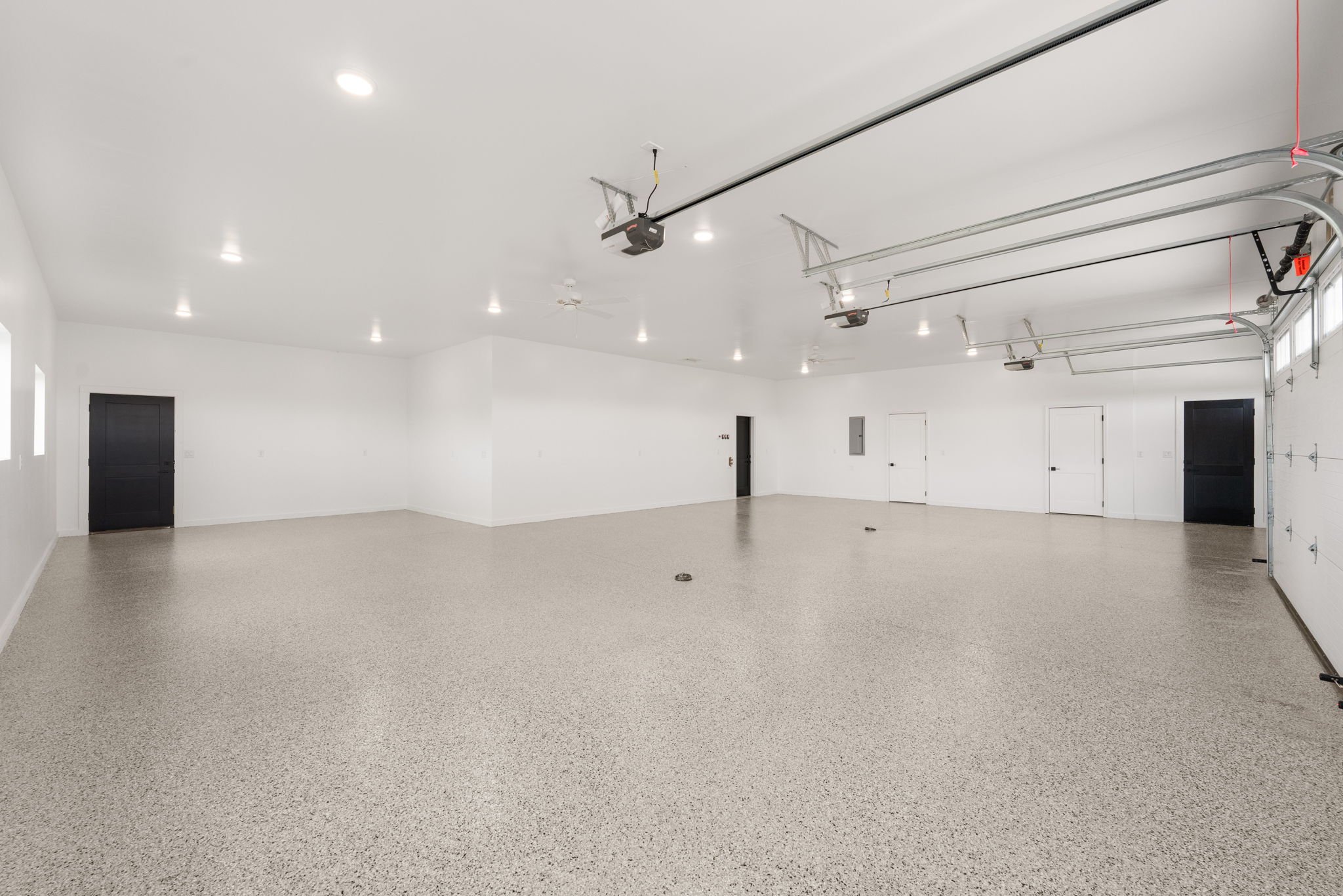 A spacious, empty two-car garage with white walls and ceiling, walled storage cabinets, and a garage door with an automatic opener.