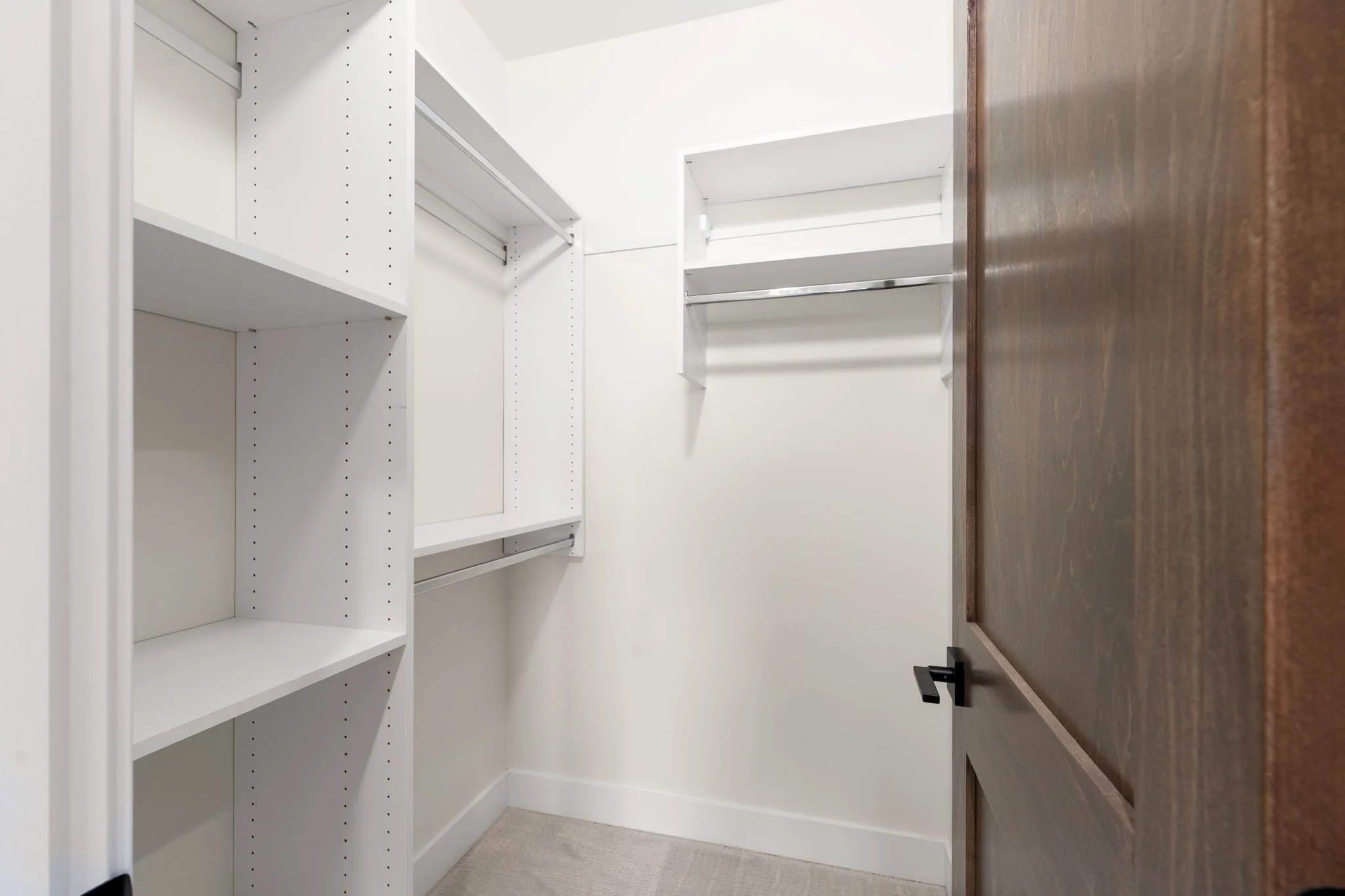 Empty walk-in closet with white walls, white shelving, and a dark wood dresser.