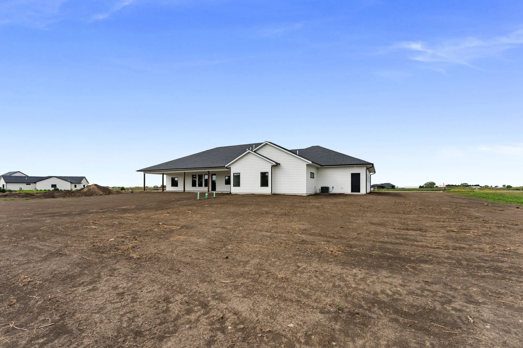 New white house with a black roof under a blue sky in a developing neighborhood, with cleared land in the foreground.