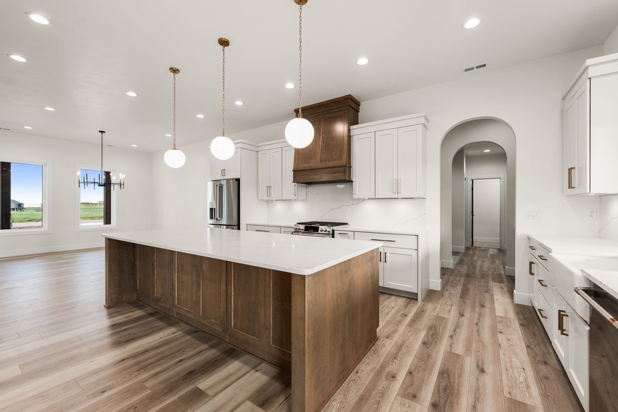 Modern kitchen with white cabinets, a large island with a wood finish, pendant lights, stainless steel appliances, and wood flooring.