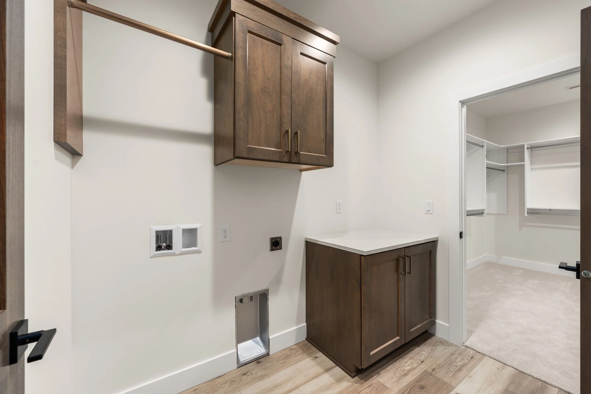 Empty laundry room with wooden cabinets, a countertop, and a closet with wire shelving.