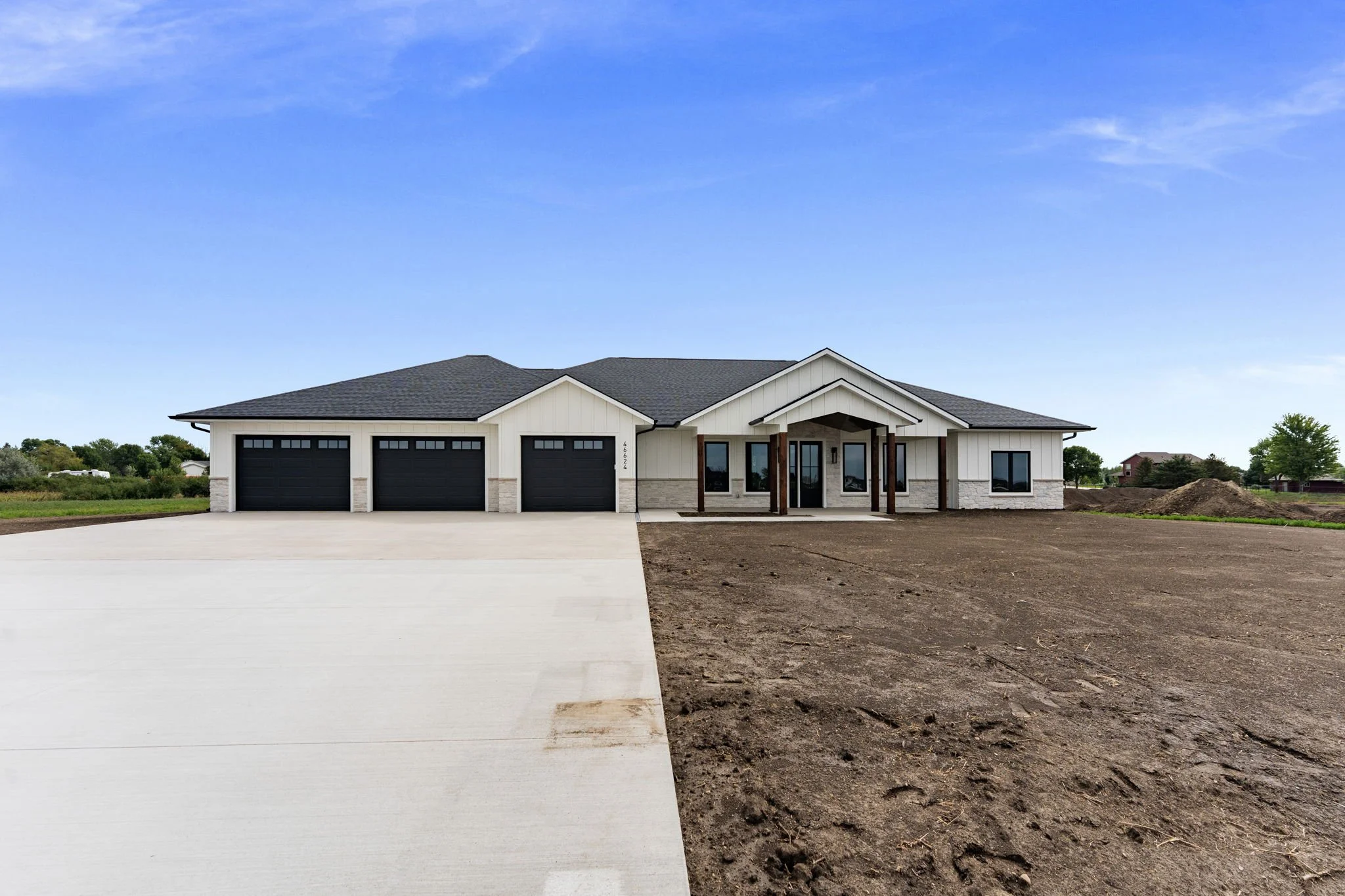 A modern house with a white exterior, dark grey garage doors, a covered porch, and a well-maintained driveway, under a bright blue sky.