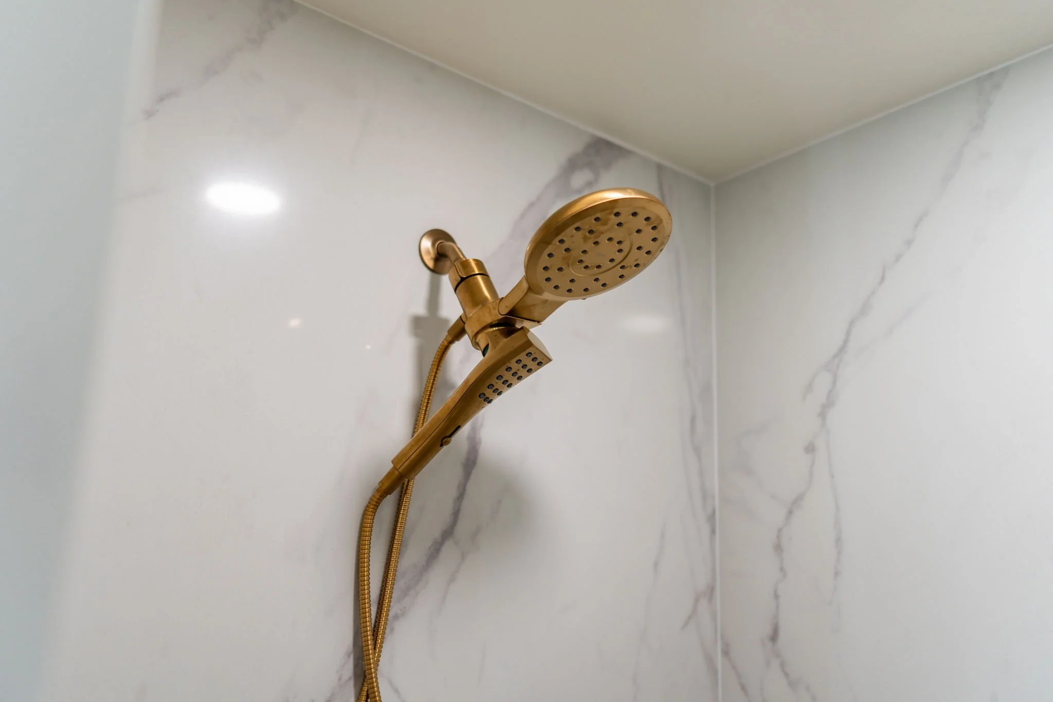 A gold-colored showerhead mounted on a white marble wall in a bathroom.