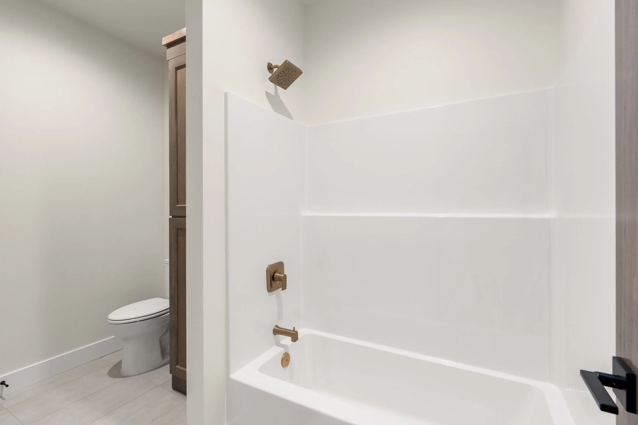 Bathroom with a white bathtub and gold fixtures, a wall-mounted showerhead, and a toilet partially visible behind a wall.