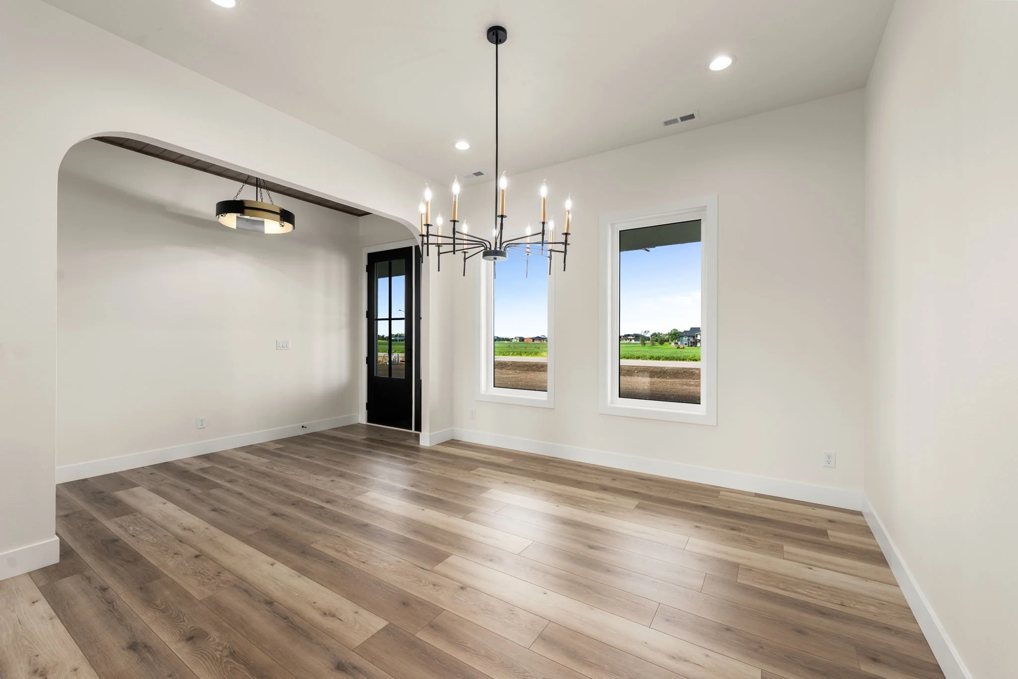 Empty room with white walls, large windows, a chandelier, and wood flooring.