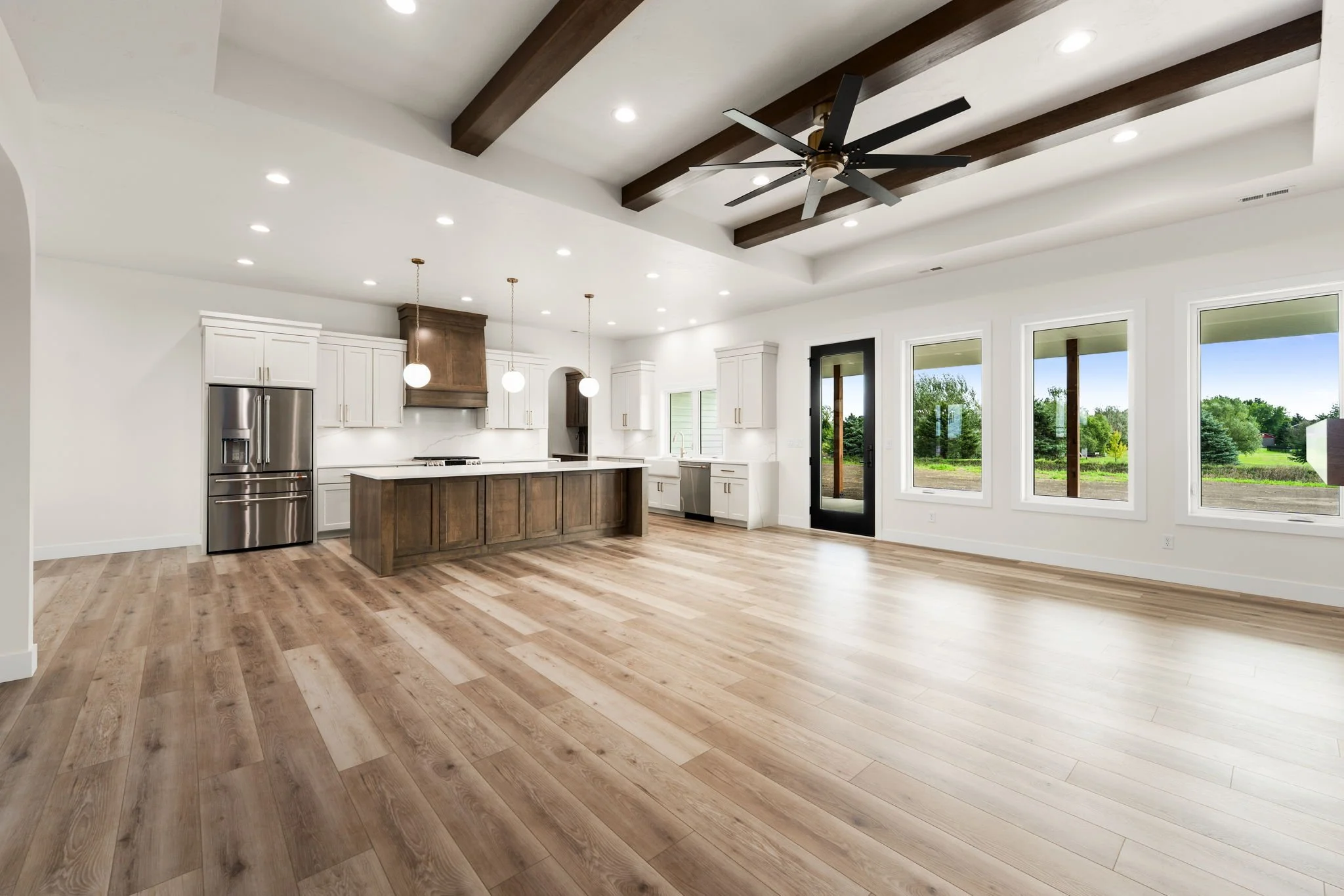 Open-concept kitchen and living area in a modern home with hardwood floors, white cabinets, a kitchen island, large windows, and a view of a backyard.