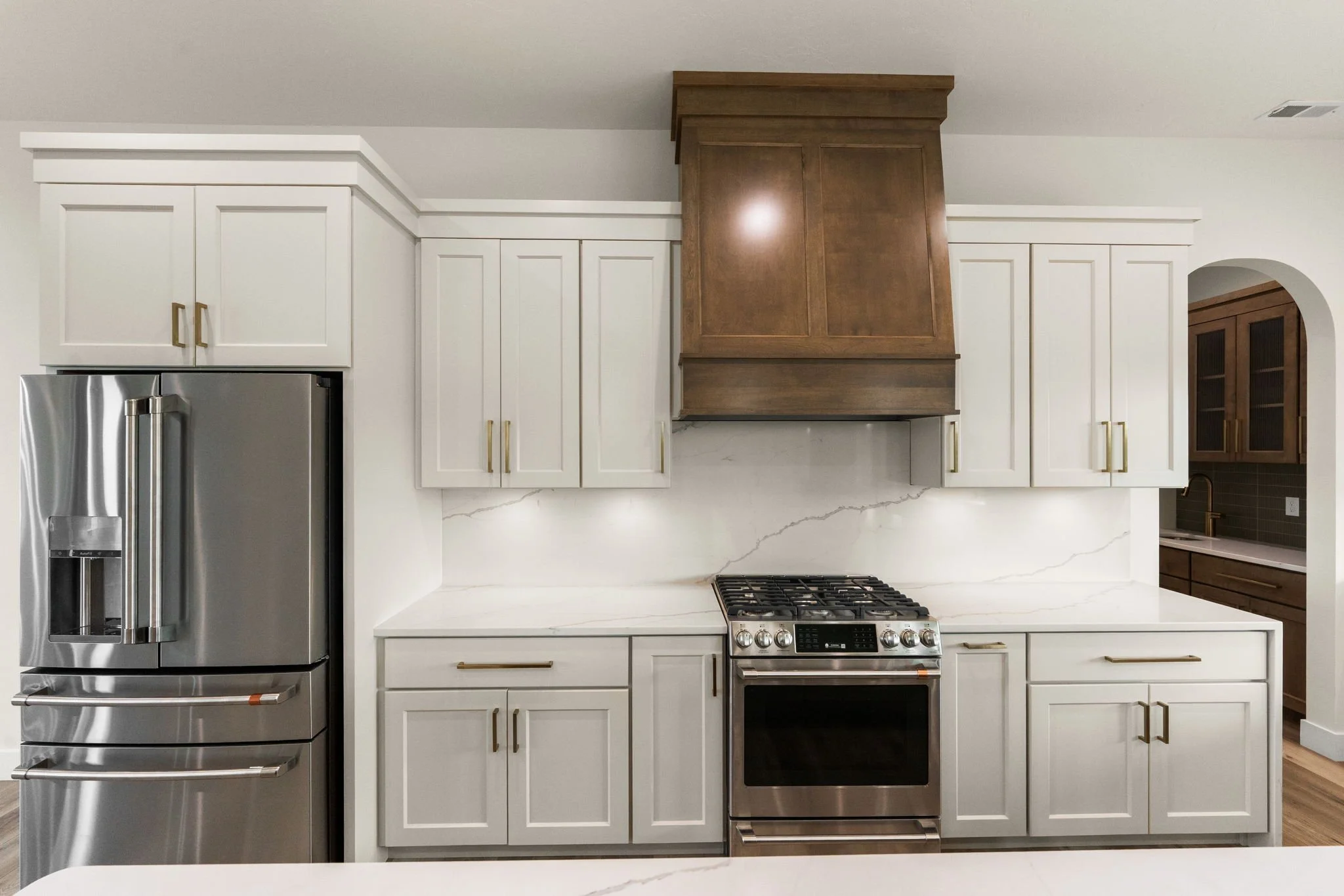 Modern kitchen with white cabinets, stainless steel refrigerator, and wooden range hood over a stove.