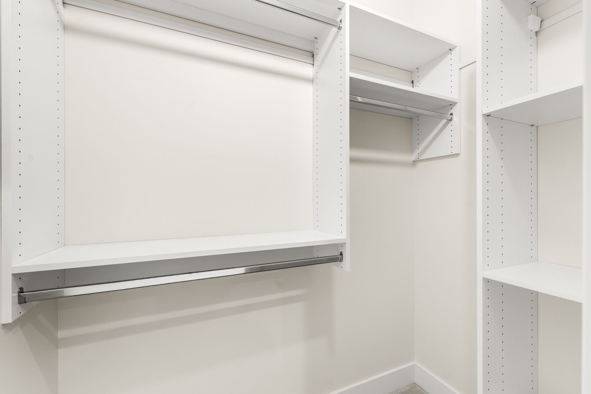 Empty white closet with adjustable shelves and clothing rods.