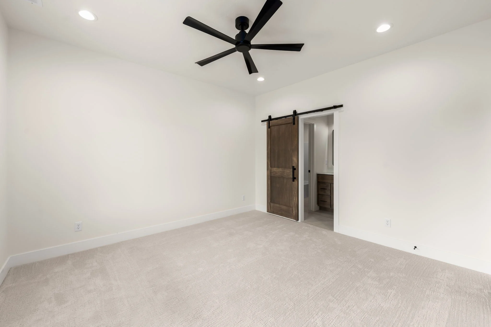 Empty bedroom with white walls, beige carpet, and a ceiling fan.