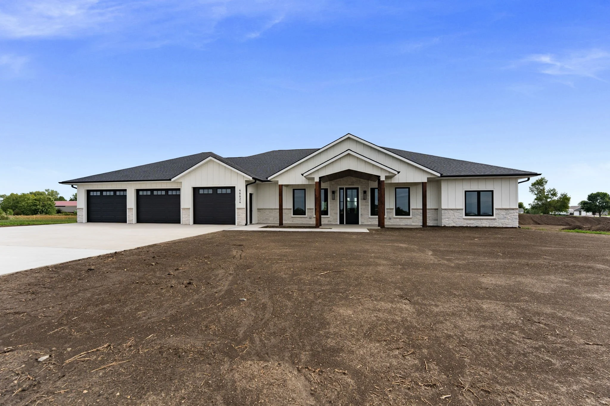 Newly constructed modern house with three garage doors, a front porch with wooden columns, and a driveway, under a blue sky.