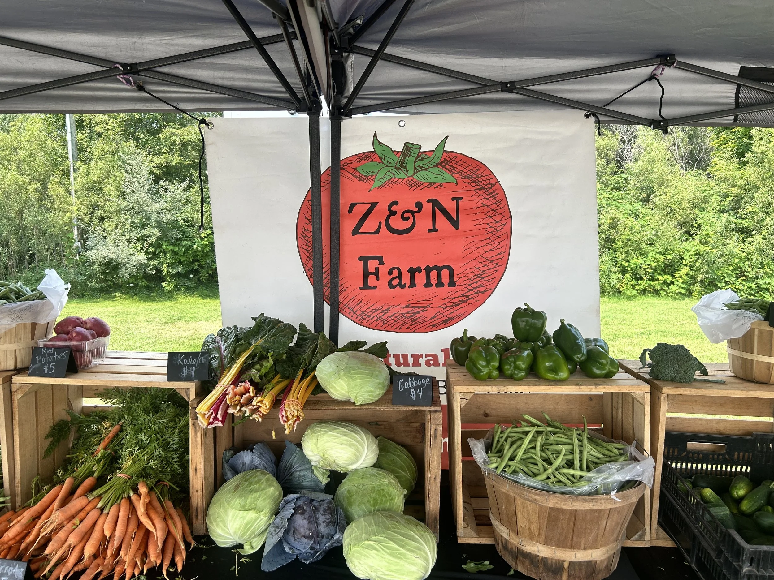 Fresh produce displayed at the farmers market with a Z&N Farm banner in the background