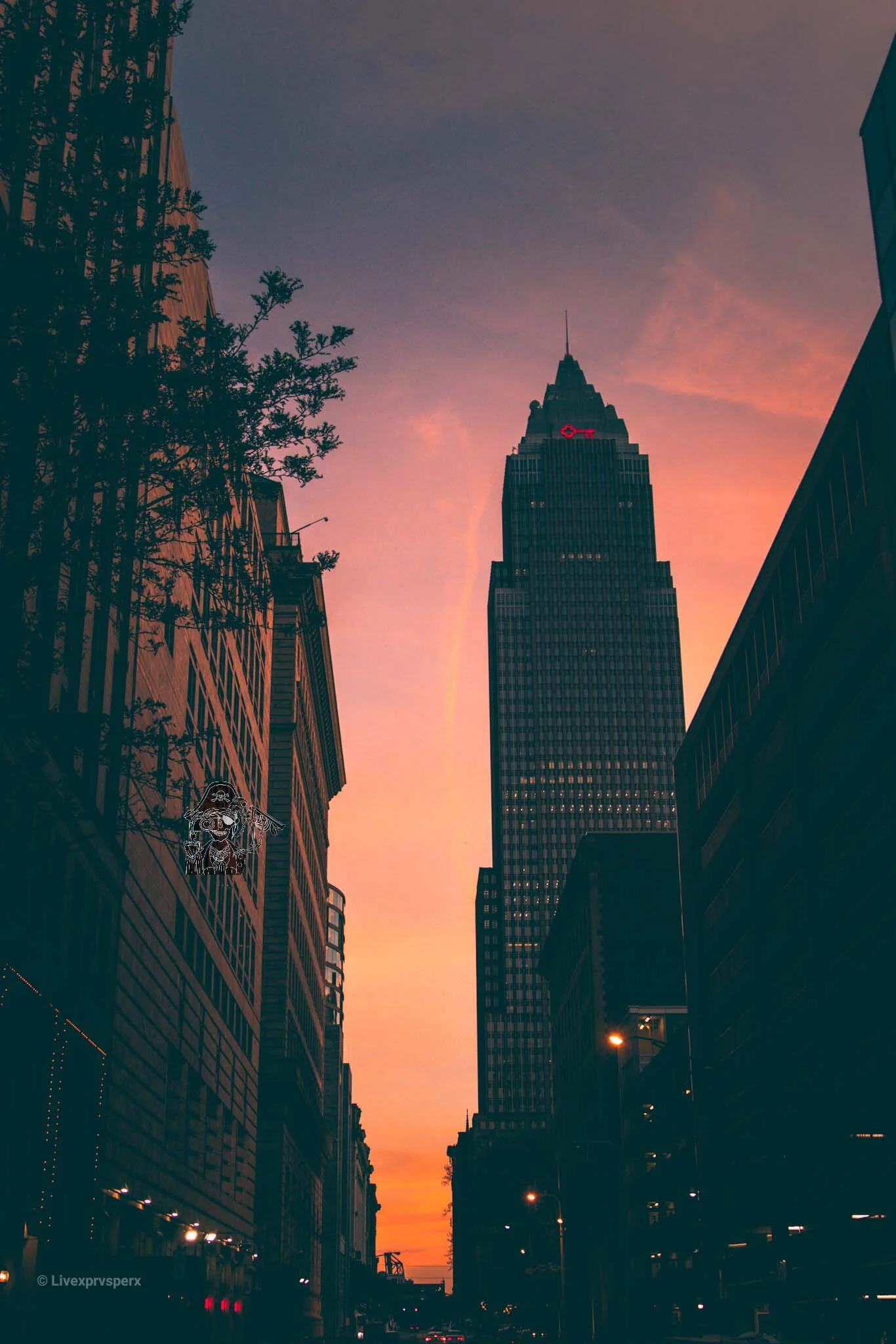 Cityscape at sunset with tall skyscrapers and a colorful sky, including a prominent building with a red lightning bolt symbol on it.