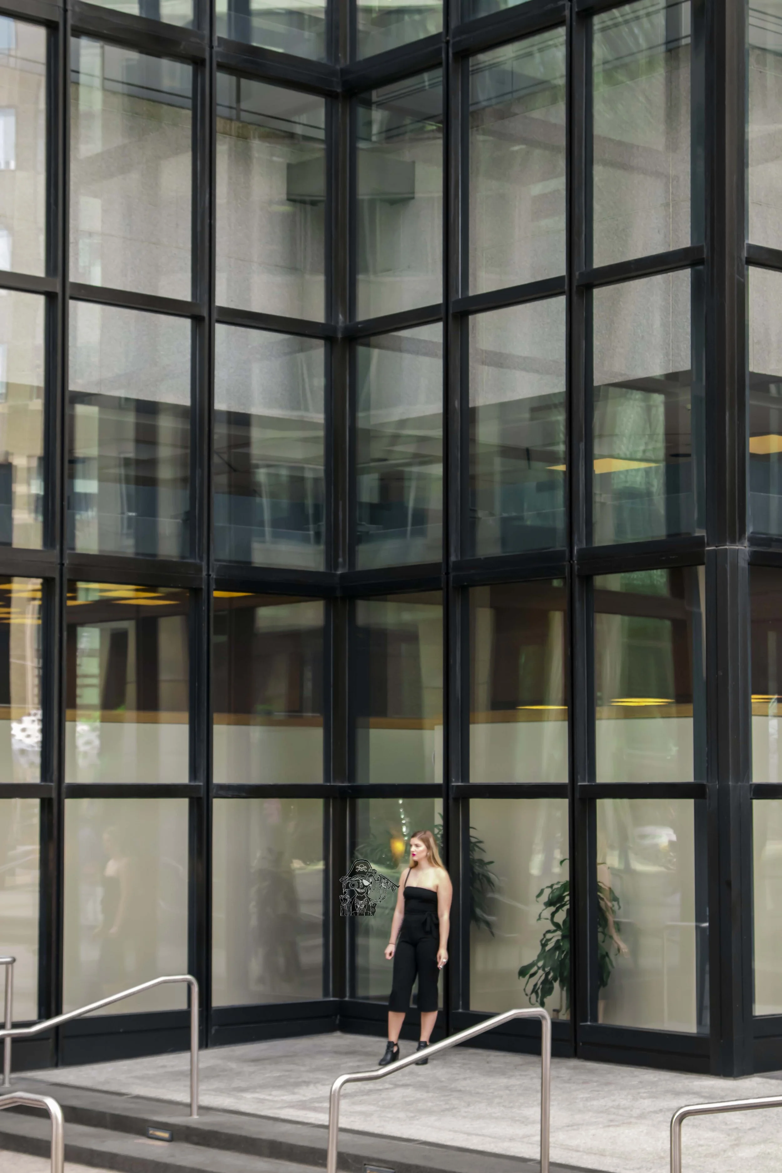 A woman in black clothing standing outside a glass building with large reflective windows.