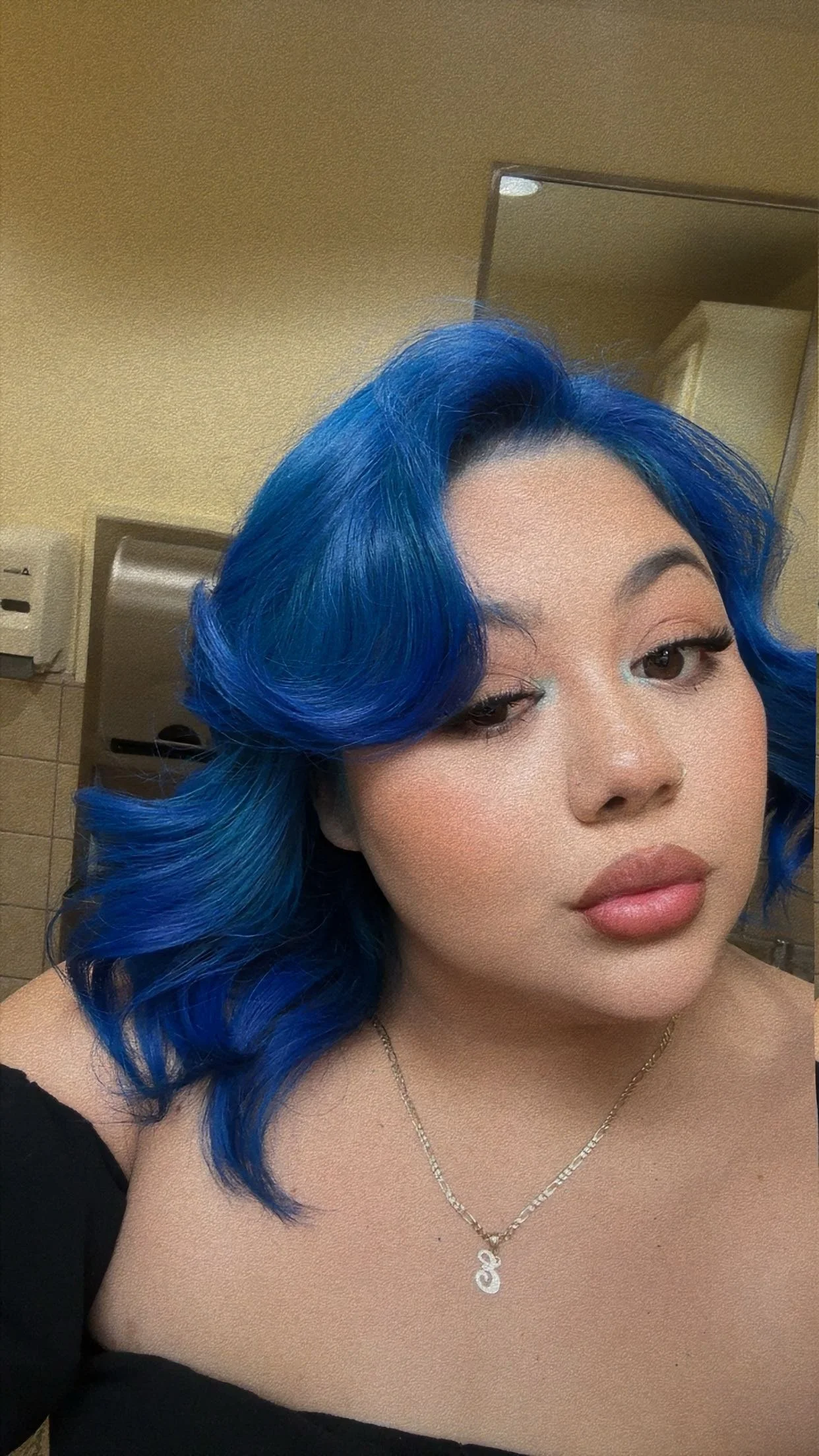 A modern wooden house with a large glass window is set in a mountainous landscape with tall, rugged mountains in the background. The house is surrounded by grassy flora and small trees.