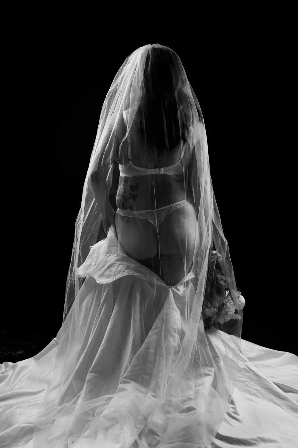 black and white bridal boudoir image showing back of wedding dress and veil
