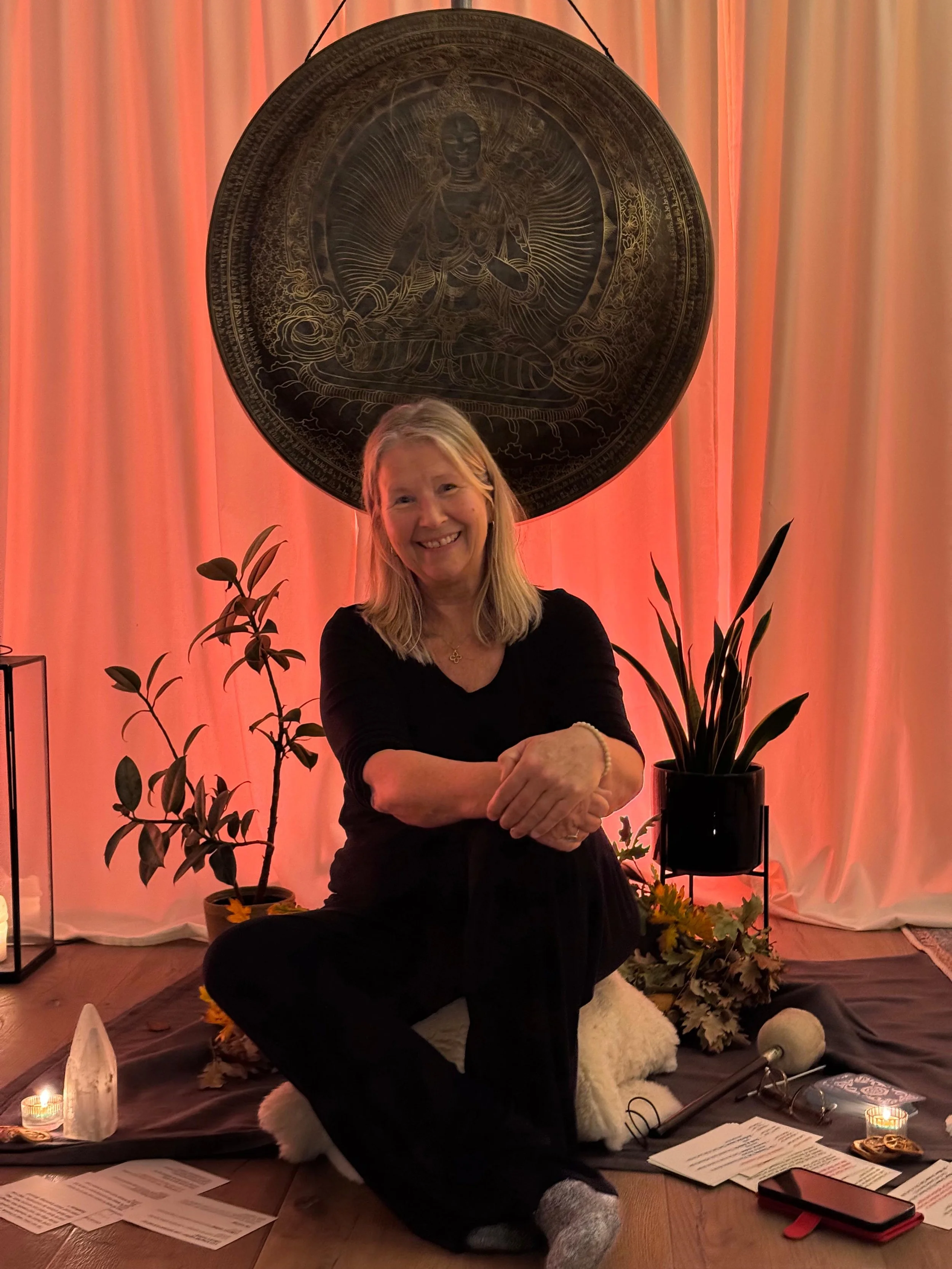 Orange background curtain and gong lady smiling with hands crossed over knee with plants in background