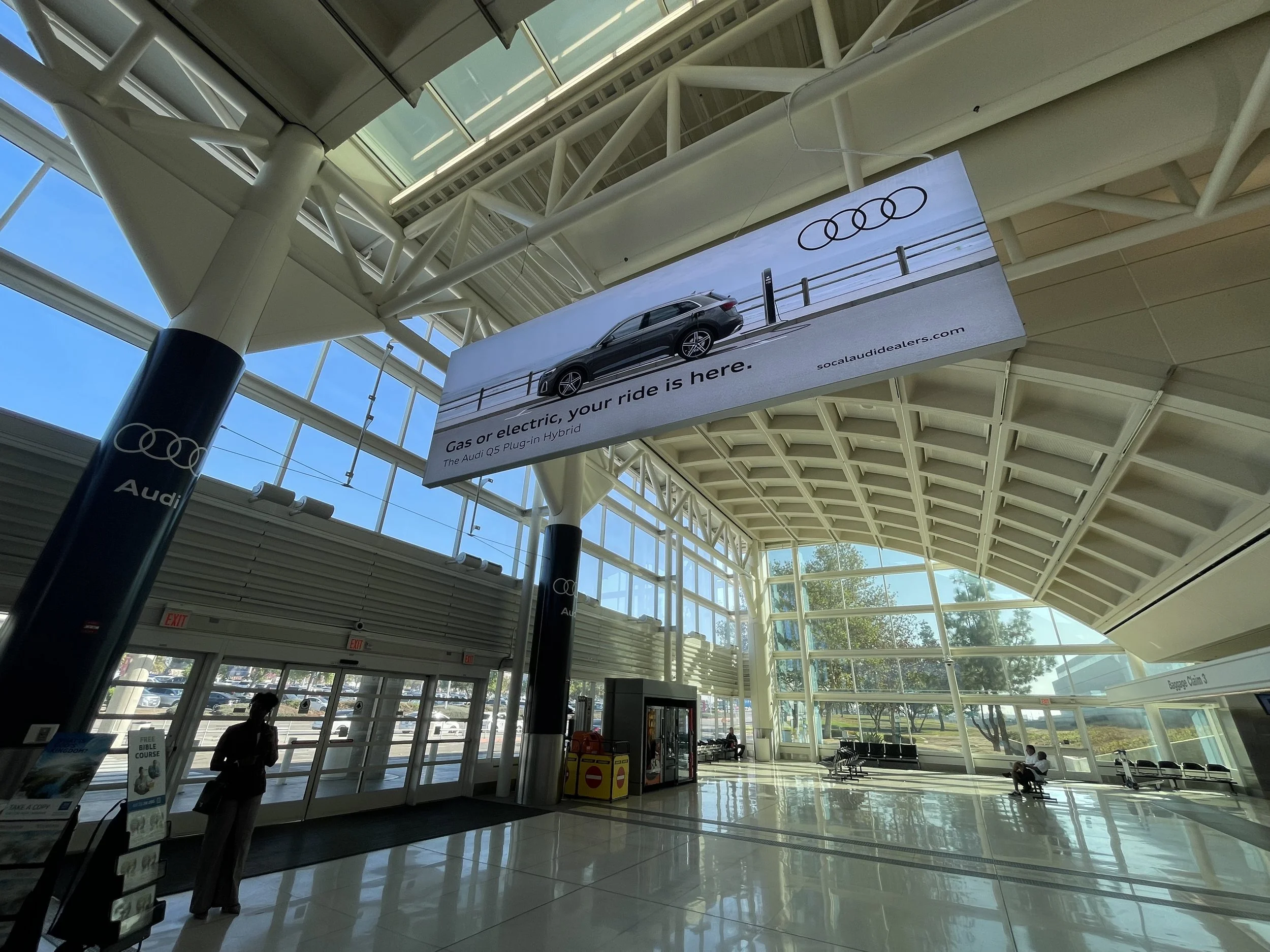 An Audi Q5 Plug-in Hybrid advertising display inside Ontario International Airport, featuring a large overhead banner and branded column wraps promoting SoCal Audi dealers in the terminal's baggage claim area.