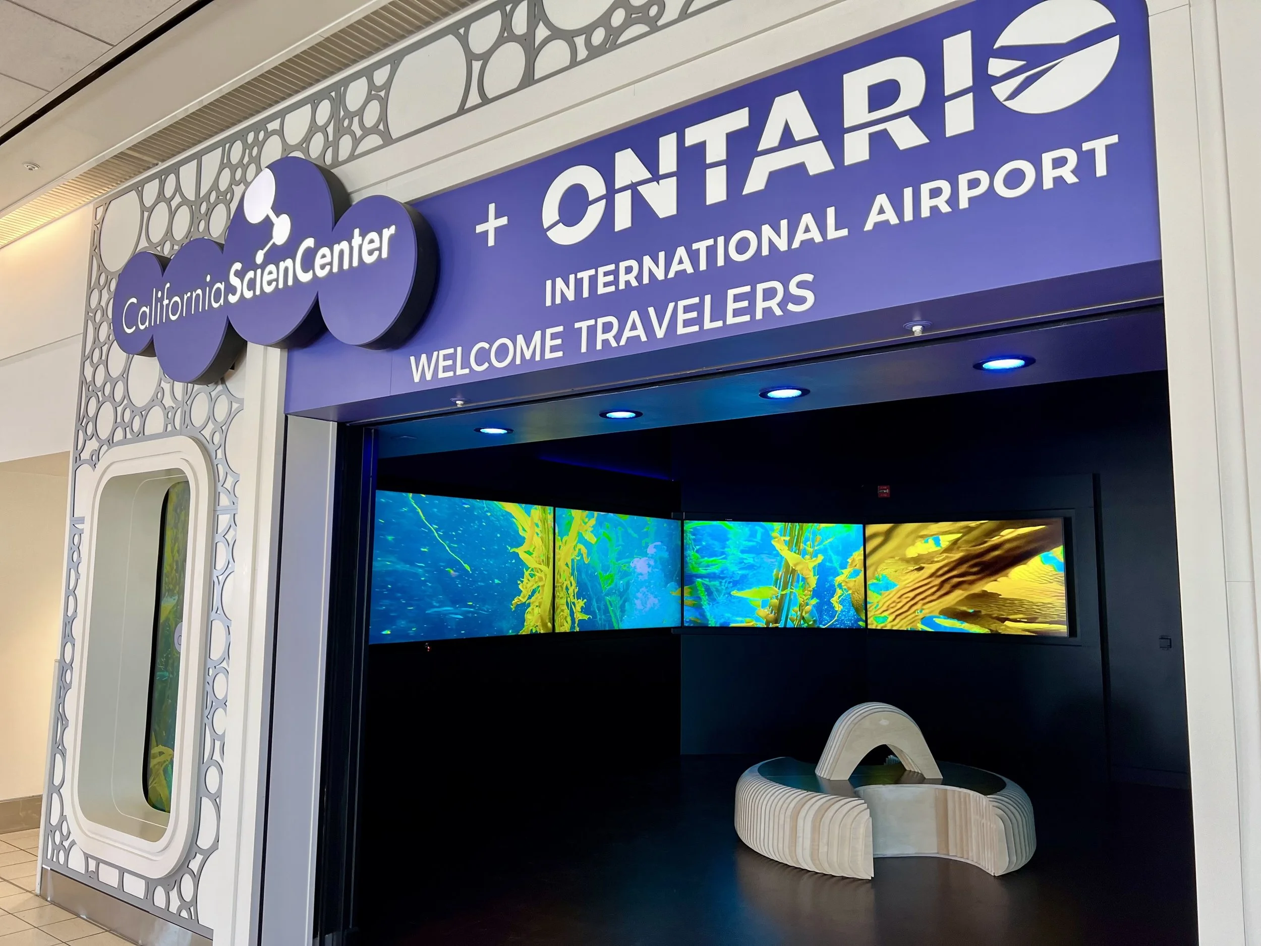 The signed entrance to the California Science Center immersive ocean experience at Ontario International Airport, with kelp forest video panels visible inside the installation.