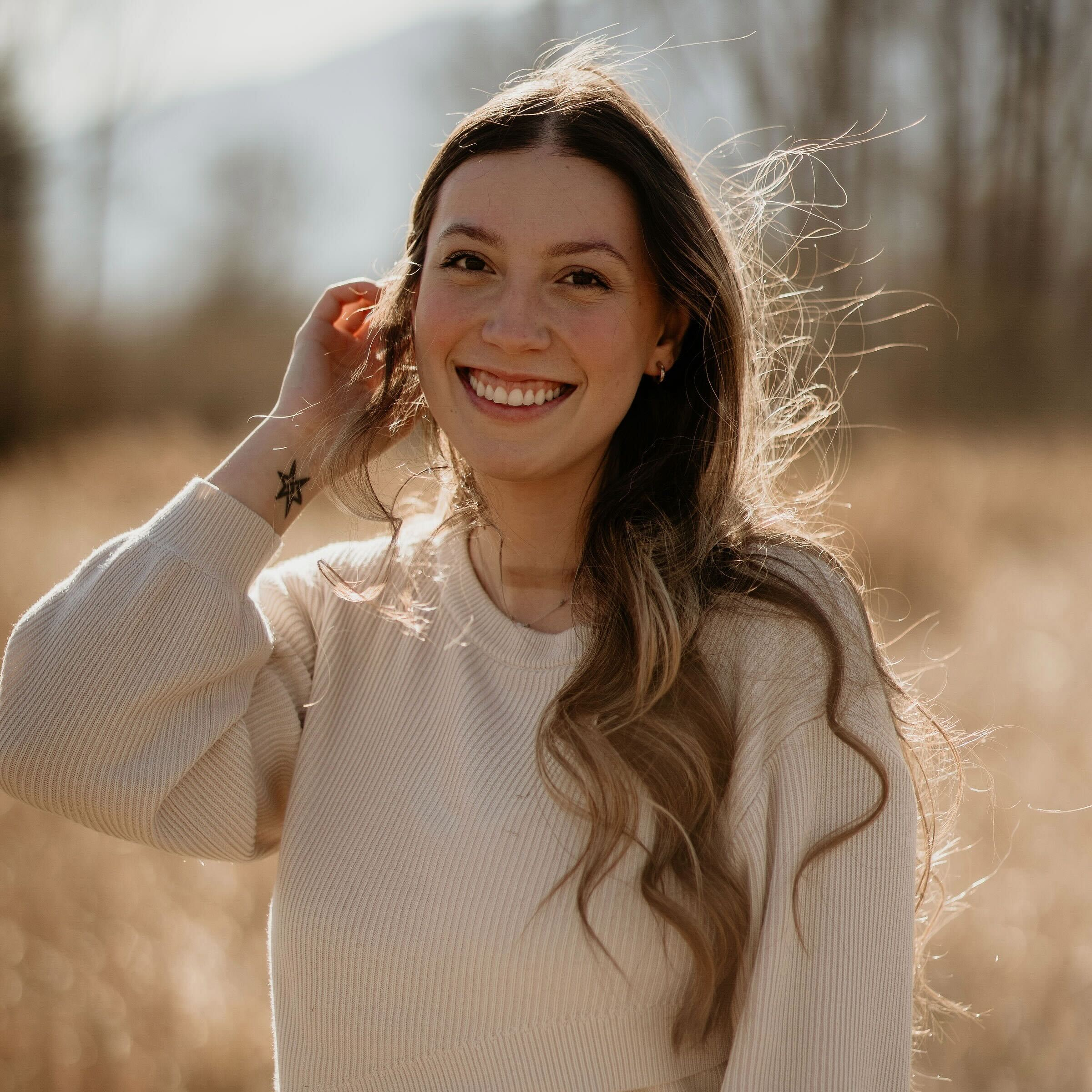 Smiling young woman hugging a fluffy brown and white dog outdoors in a natural setting.