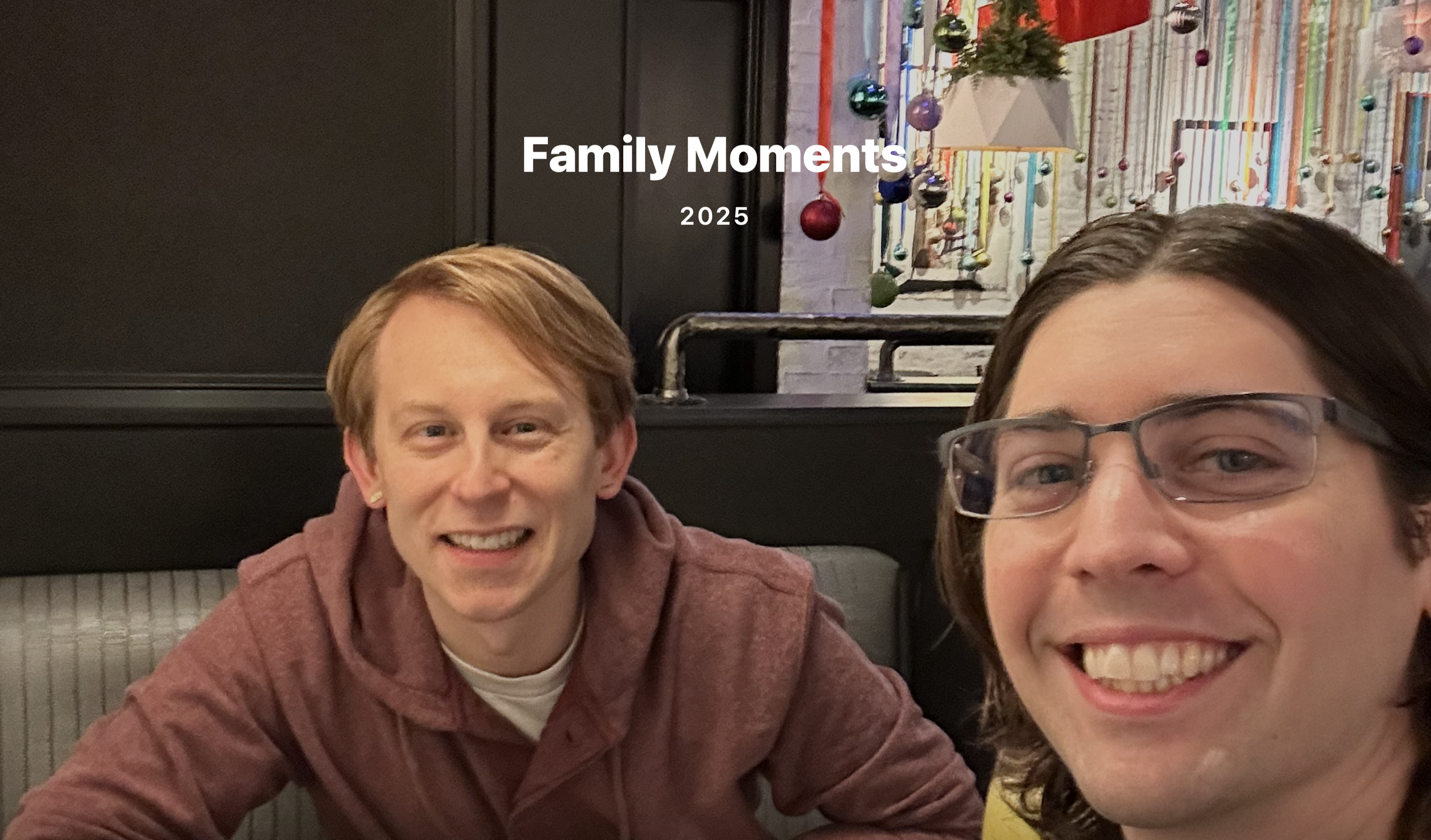 Two young men smiling at a restaurant or café, with Christmas decor hanging on the wall behind them.