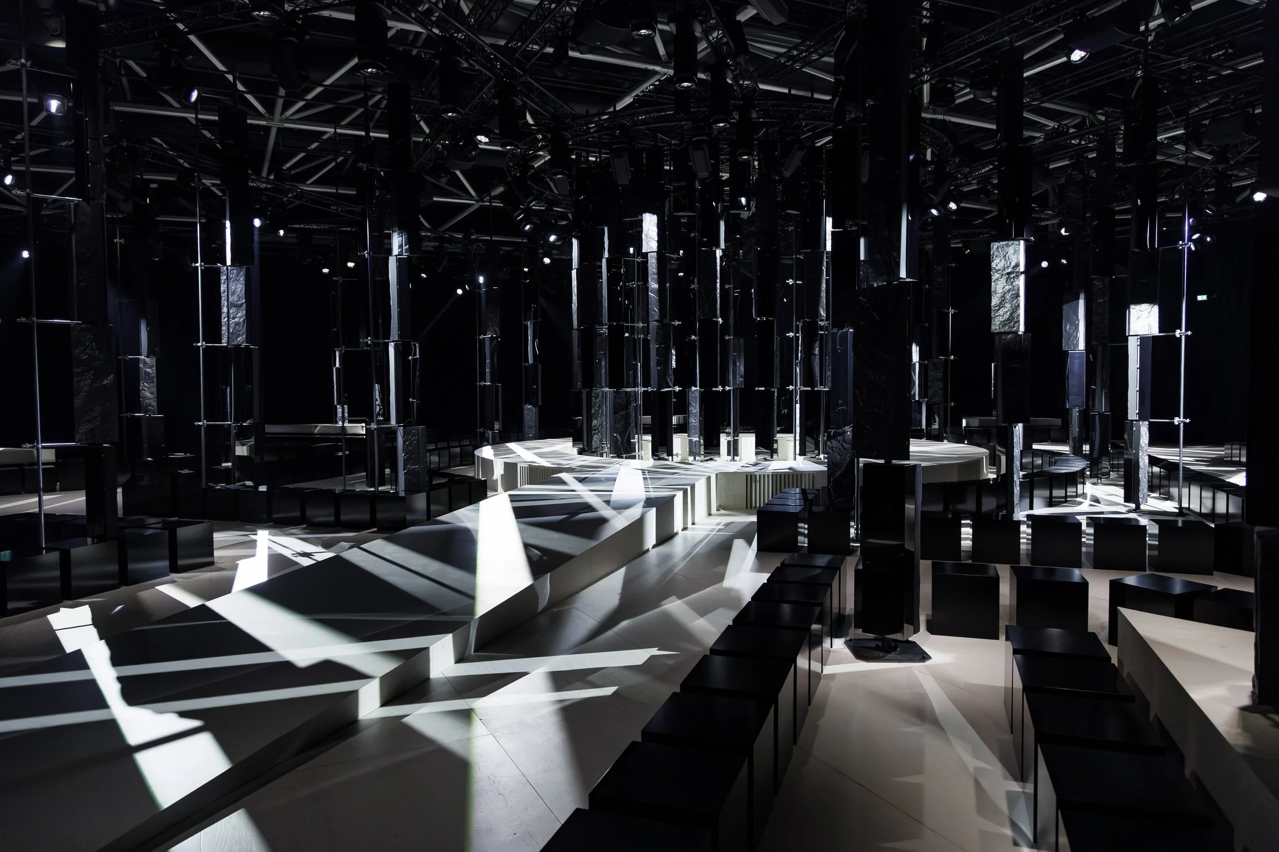 Black runway with white light and mirrored columns, Givenchy Fall/Winter 2026 show, Sarah Burton. Set design by James Chinlund.