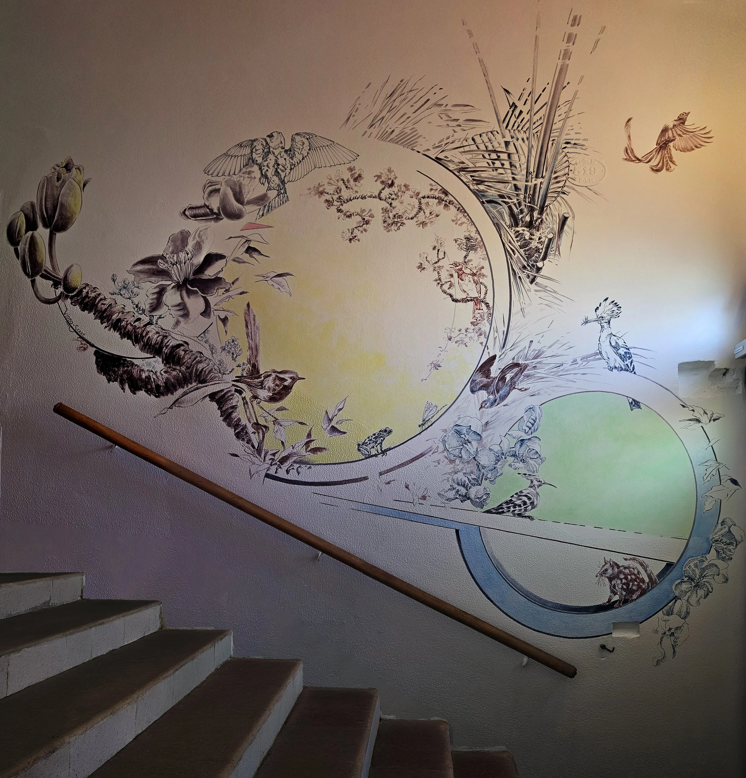 Das Bild zeigt eine leichte aber dynamische Komposition mit verschiedenen Elementen aus Fauna und Flora. Das Wandbild spielt mit dem Lichteinfall und den Art Deco Elementen des Gebäudes. Farblich bindet es die bunten Glassfenster des Eingangsportals