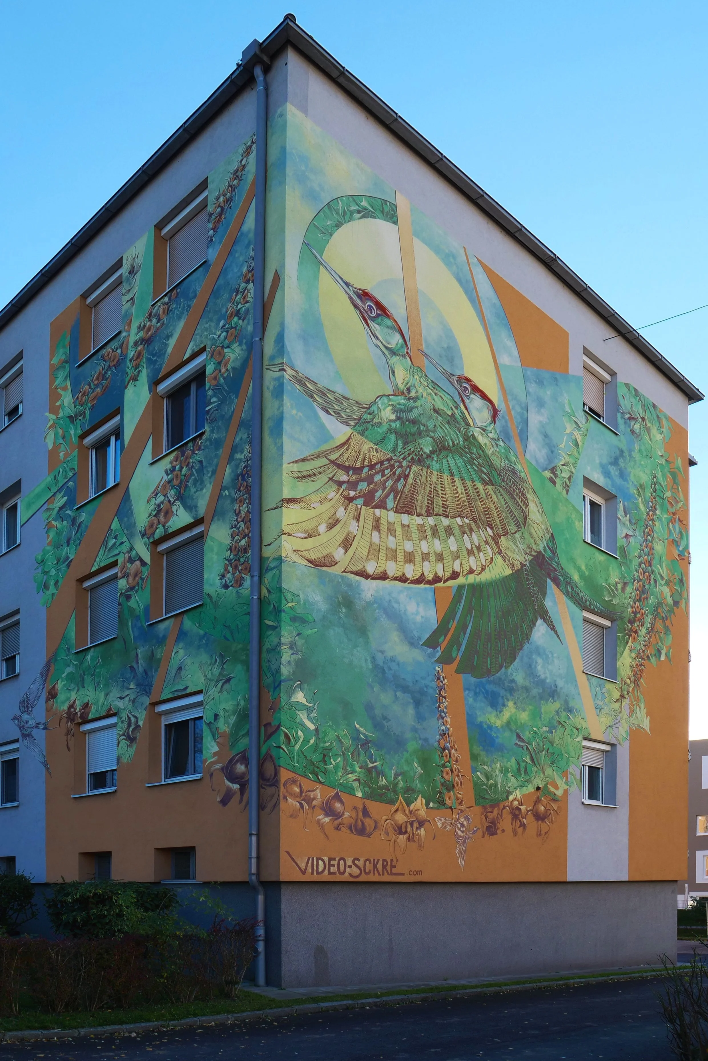 The task was to include the corner of the building within the mural. We used the original colour of the building in motives of our composition. The painted green woodpecker is a symbol  urban wildlife and nature. The mural is done ith KEIM Soldalit