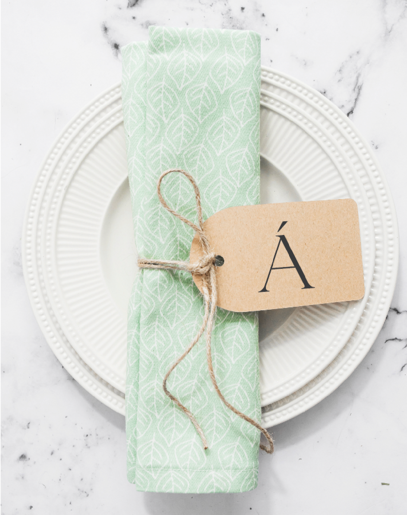 Green fabric napkin on a side plate with  brown paper tag with ÁITIÚIL's  lettermark, a single A