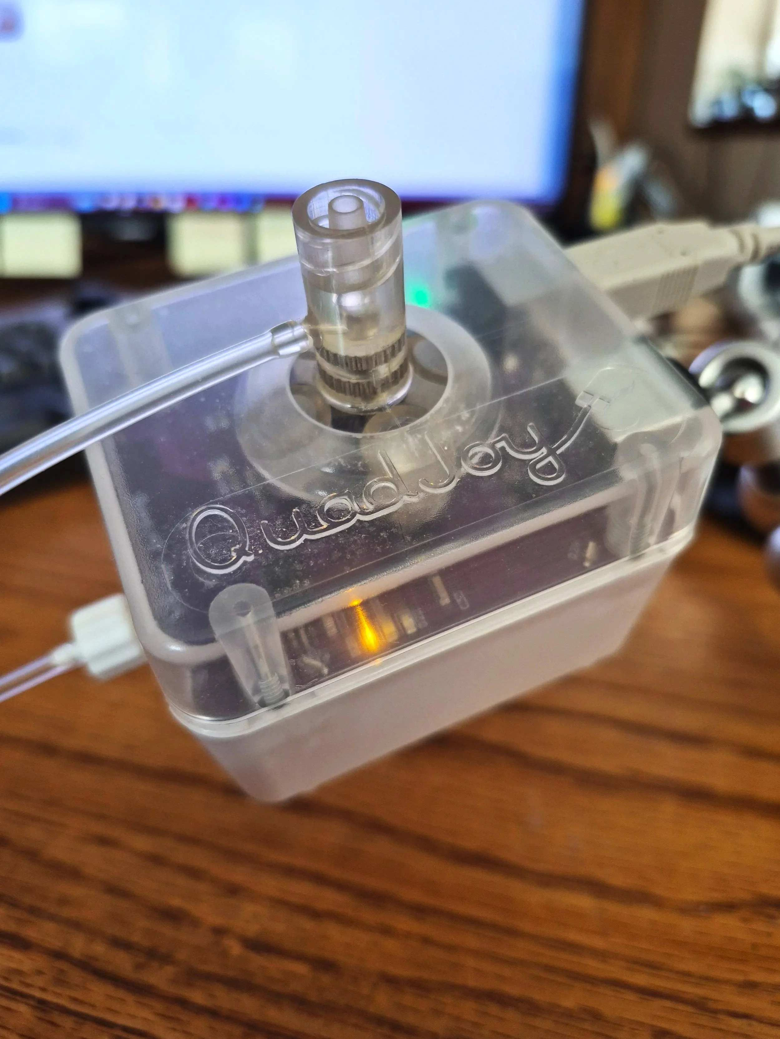 Close-up of a medical device with a transparent connector, connected to a tube, placed on a wooden surface in front of a computer monitor.