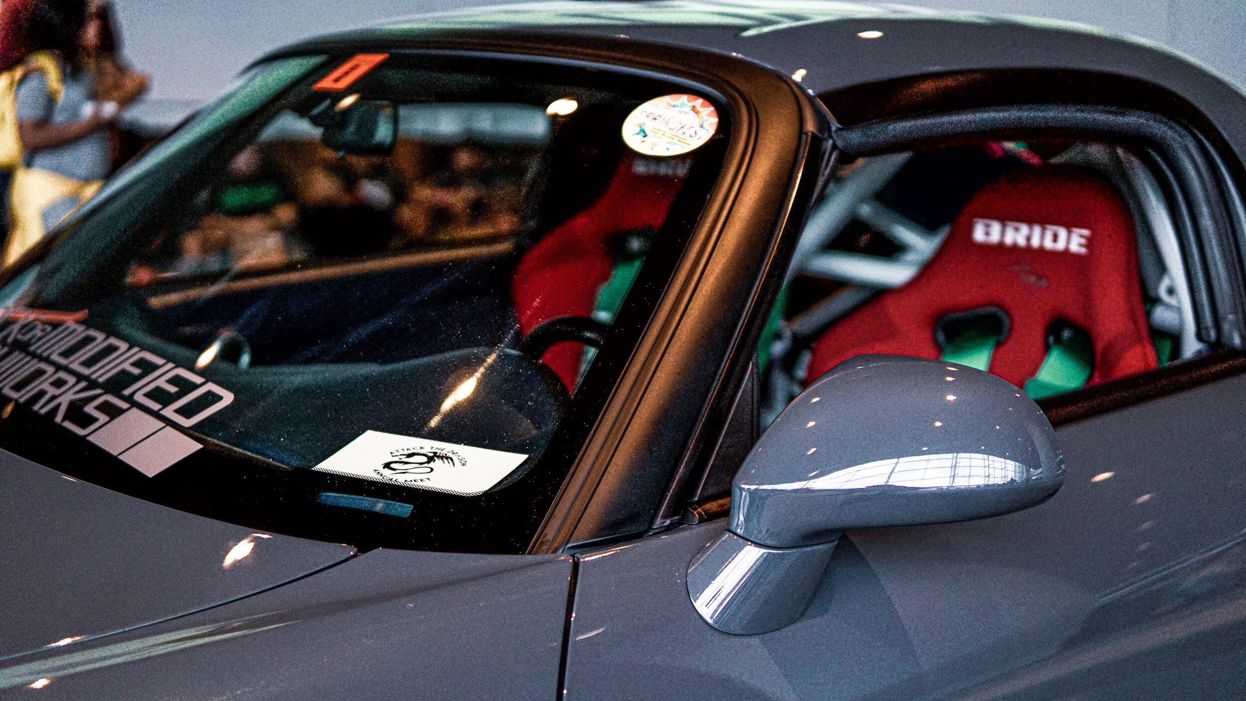 Close-up of a gray sports car with a red racing seat and a sticker on the windshield that reads 'Unmodified Works'