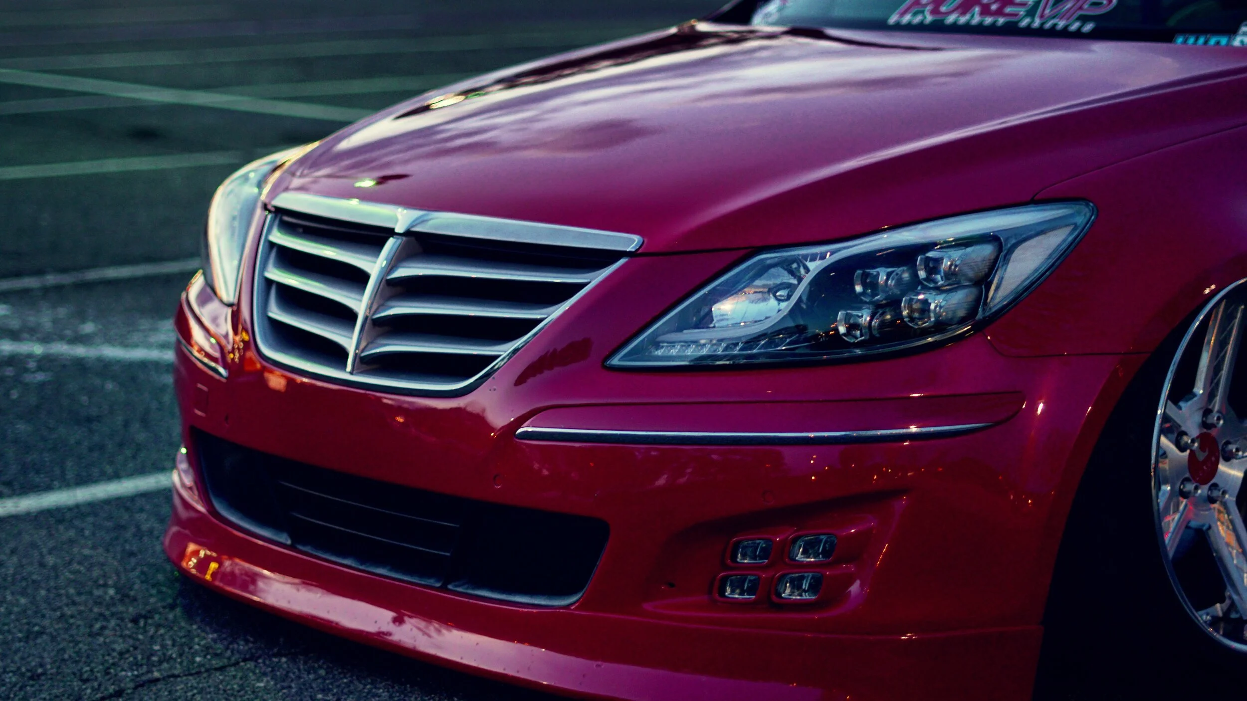 Close-up of the front of a red luxury car, showing the grille, headlights, and part of the front bumper.