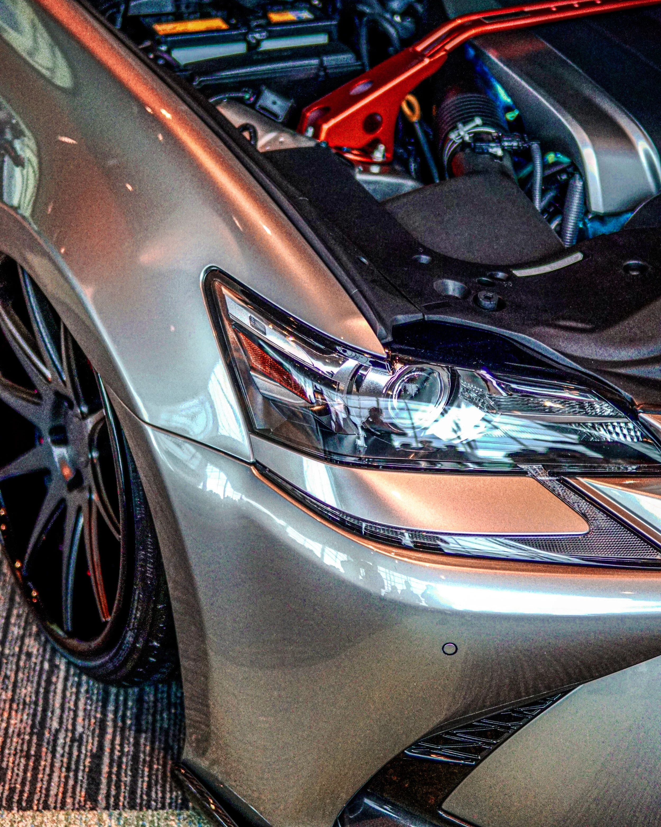 Close-up of a modern luxury sports car with its hood open, revealing engine components, parked indoors on a patterned carpet.