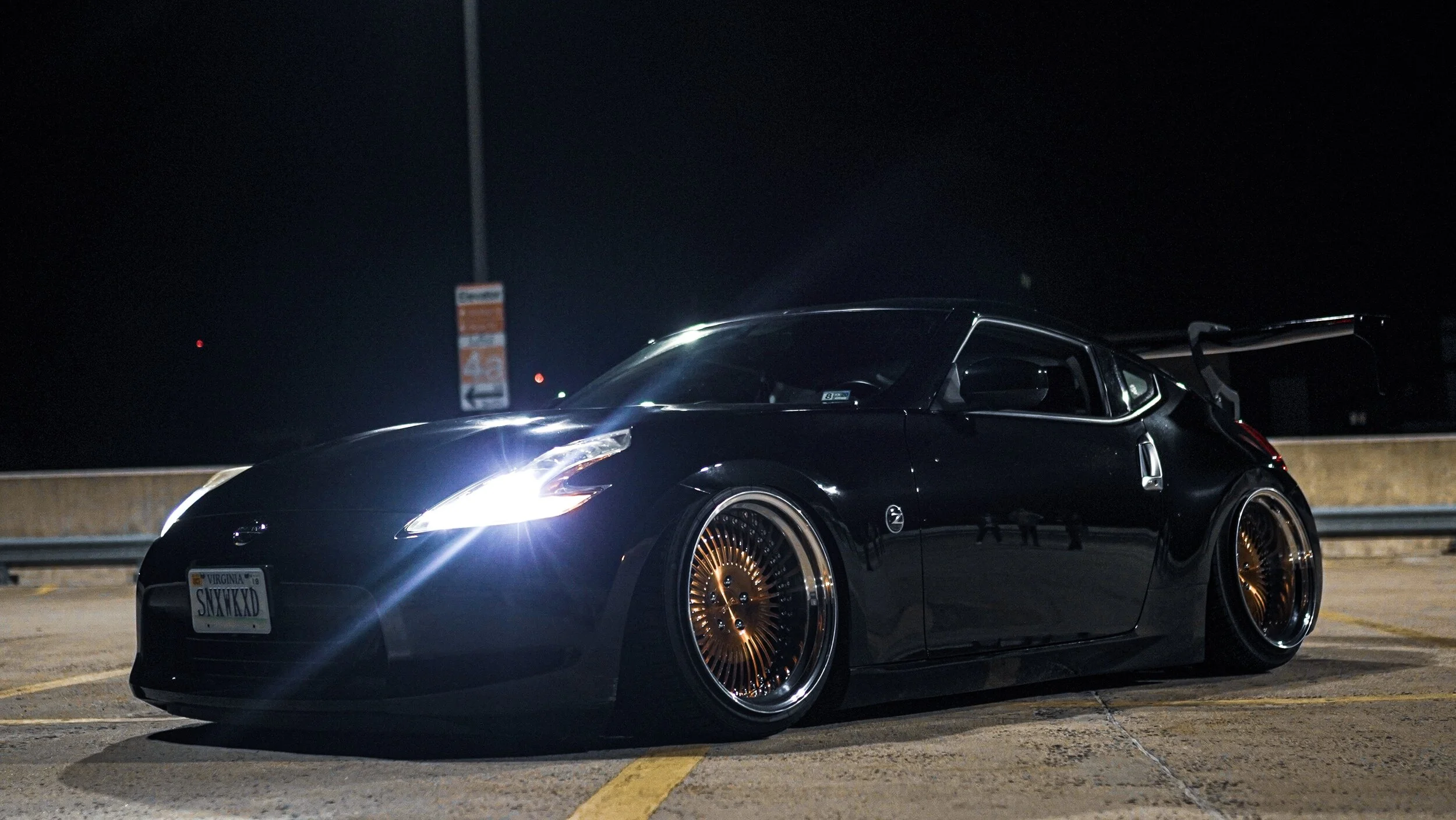 Dark sports car with custom gold wheels parked in a dimly lit lot at night.