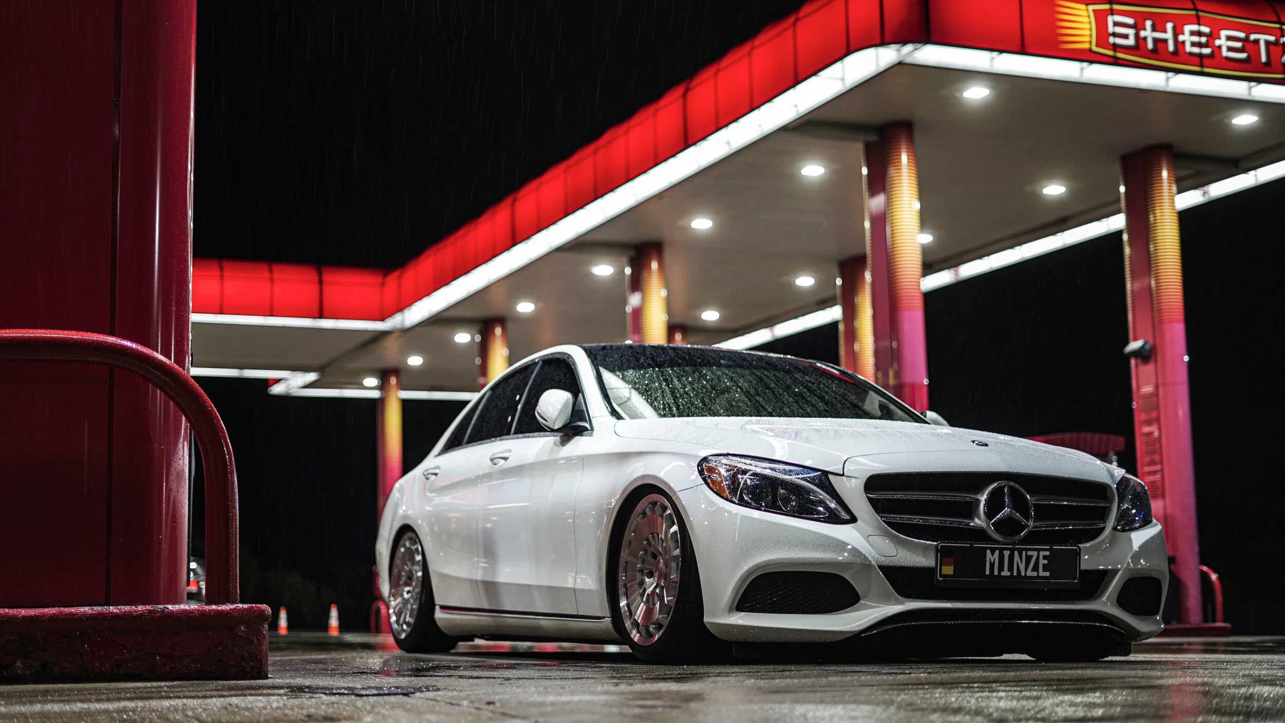 White Mercedes-Benz car at a gas station during rain at night, with red and pink lighting accents.