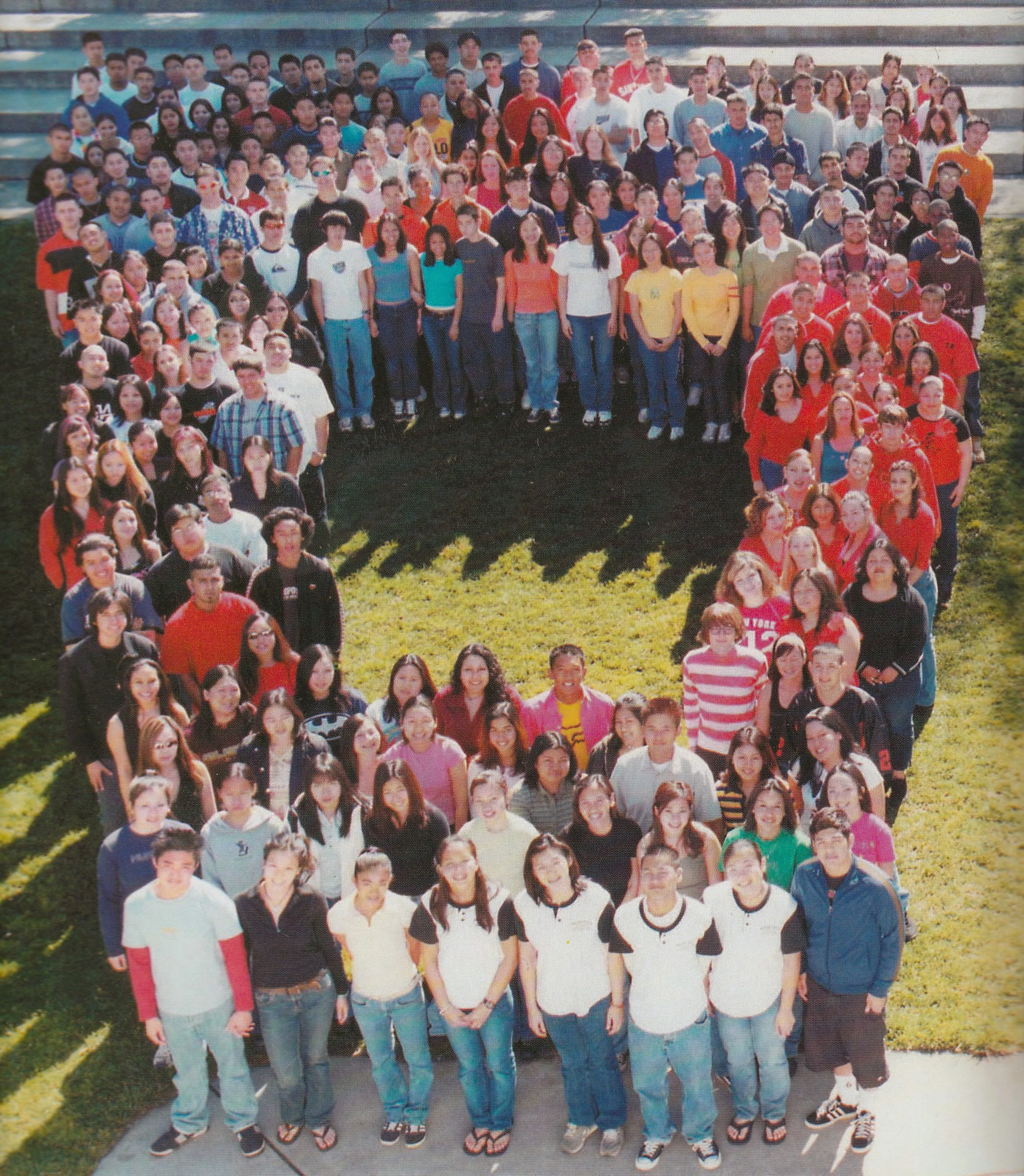 Group photo of students and teachers arranged in a heart shape on a school field outdoors.