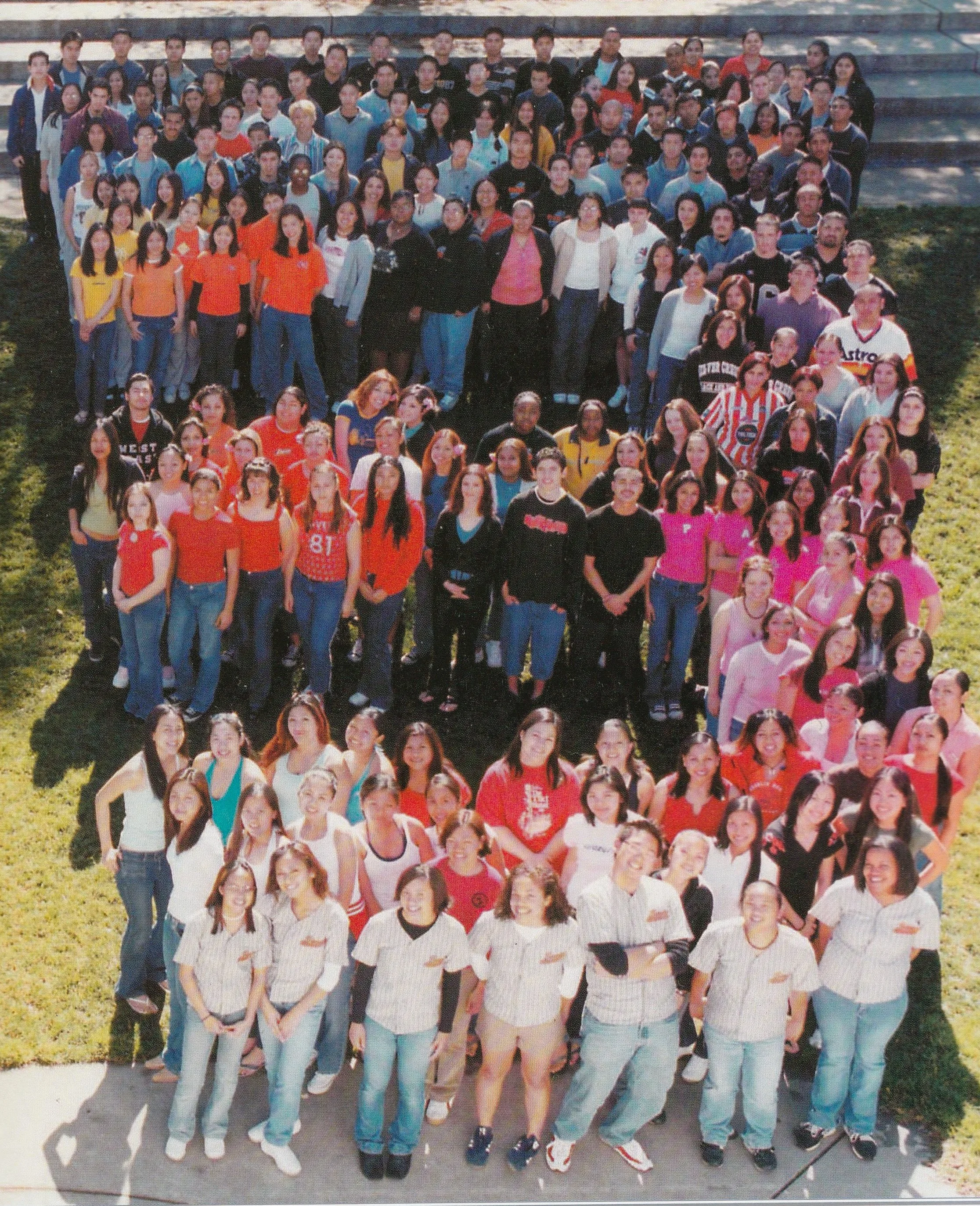 A large group of students, teachers, and staff gathered outdoors on a grassy area for a group photo, with some sitting and others standing in rows.