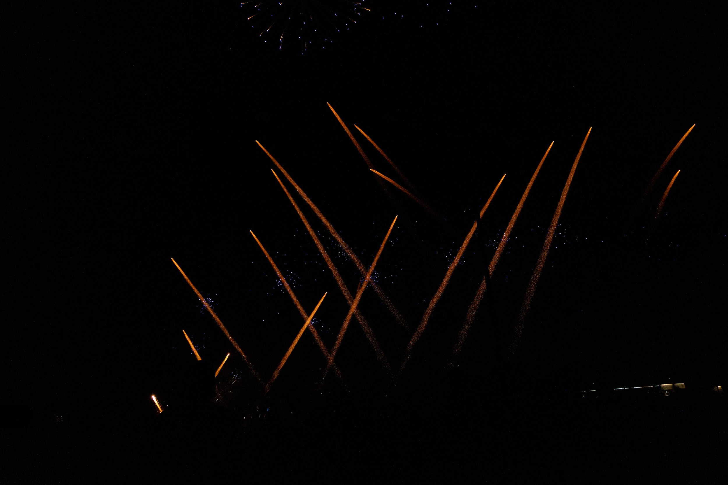 Fireworks exploding in the night sky with orange streaks and small blue and white sparks.